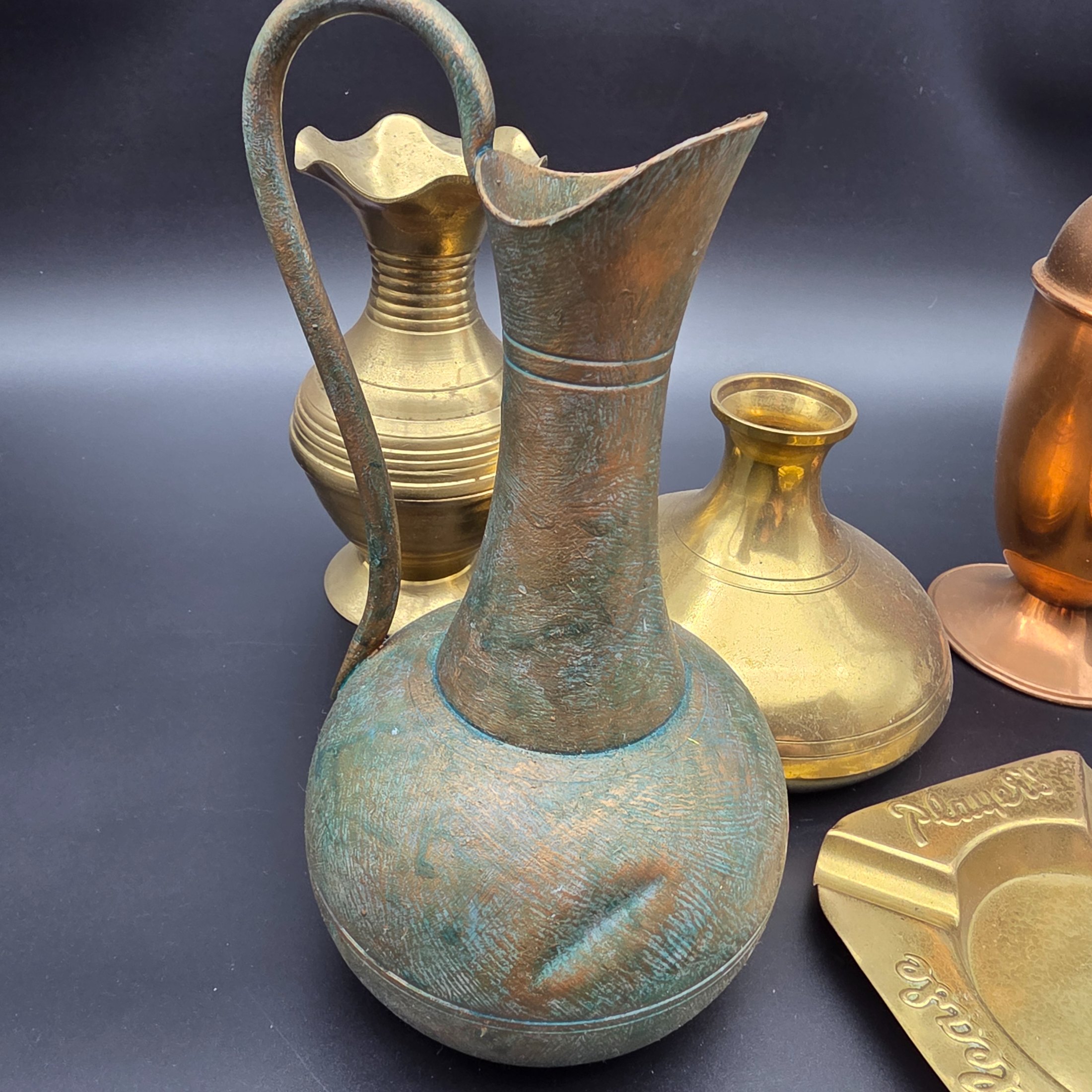 An appealing collection of eight assorted vintage brass and copper decorative items, including jugs, vases, pots, and ashtrays, showcasing varied forms and patinas from different eras and origins, ideal for display or use in period interiors. This lot includes an Australian-made Glama-Ware brass-finished stainless steel lidded pot and a 'Players' brand ashtray made in England. - View 7