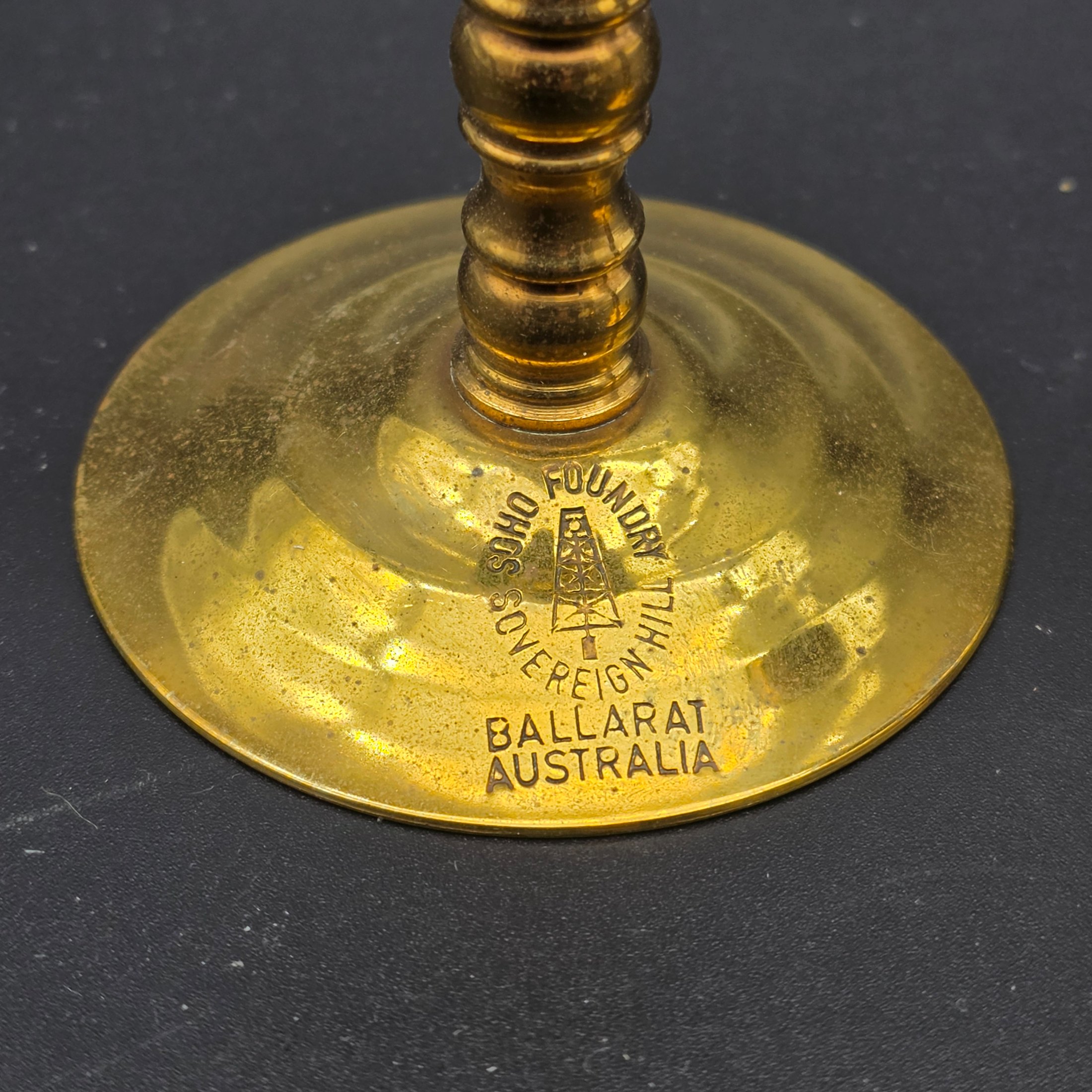 A pair of vintage brass candlesticks, stamped with "Soho Foundry Sovereign Hill Ballarat Australia" and featuring a mining derrick logo, showcasing traditional craftsmanship. - View 5