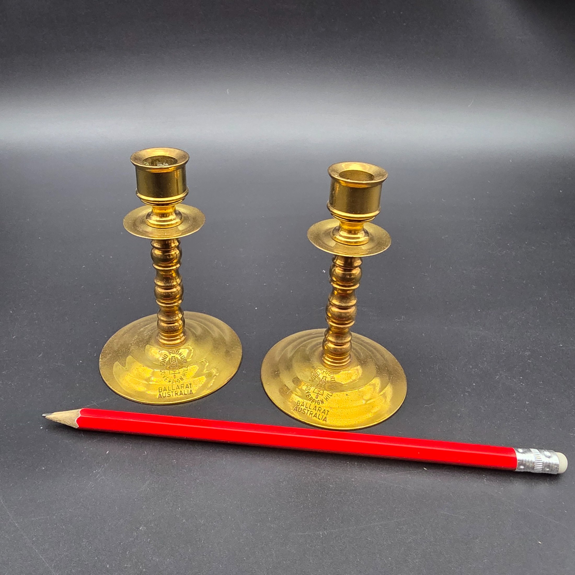 A pair of vintage brass candlesticks, stamped with "Soho Foundry Sovereign Hill Ballarat Australia" and featuring a mining derrick logo, showcasing traditional craftsmanship. - View 6