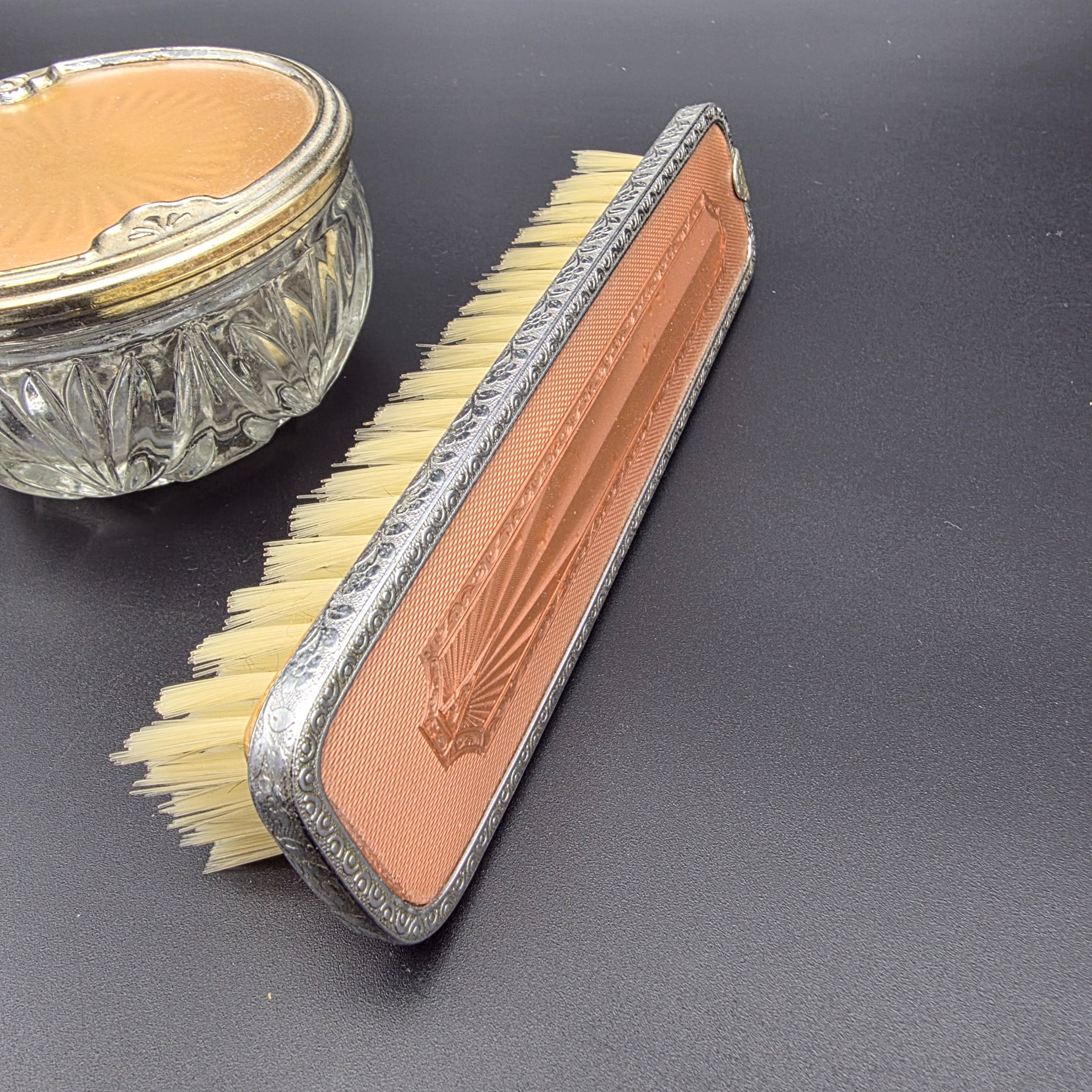 A five-piece vintage Art Deco dressing table vanity set, featuring a hand mirror, two brushes, and a lidded glass powder jar, all with silver-tone metal and rose-gold toned celluloid fan-patterned inserts. - View 2