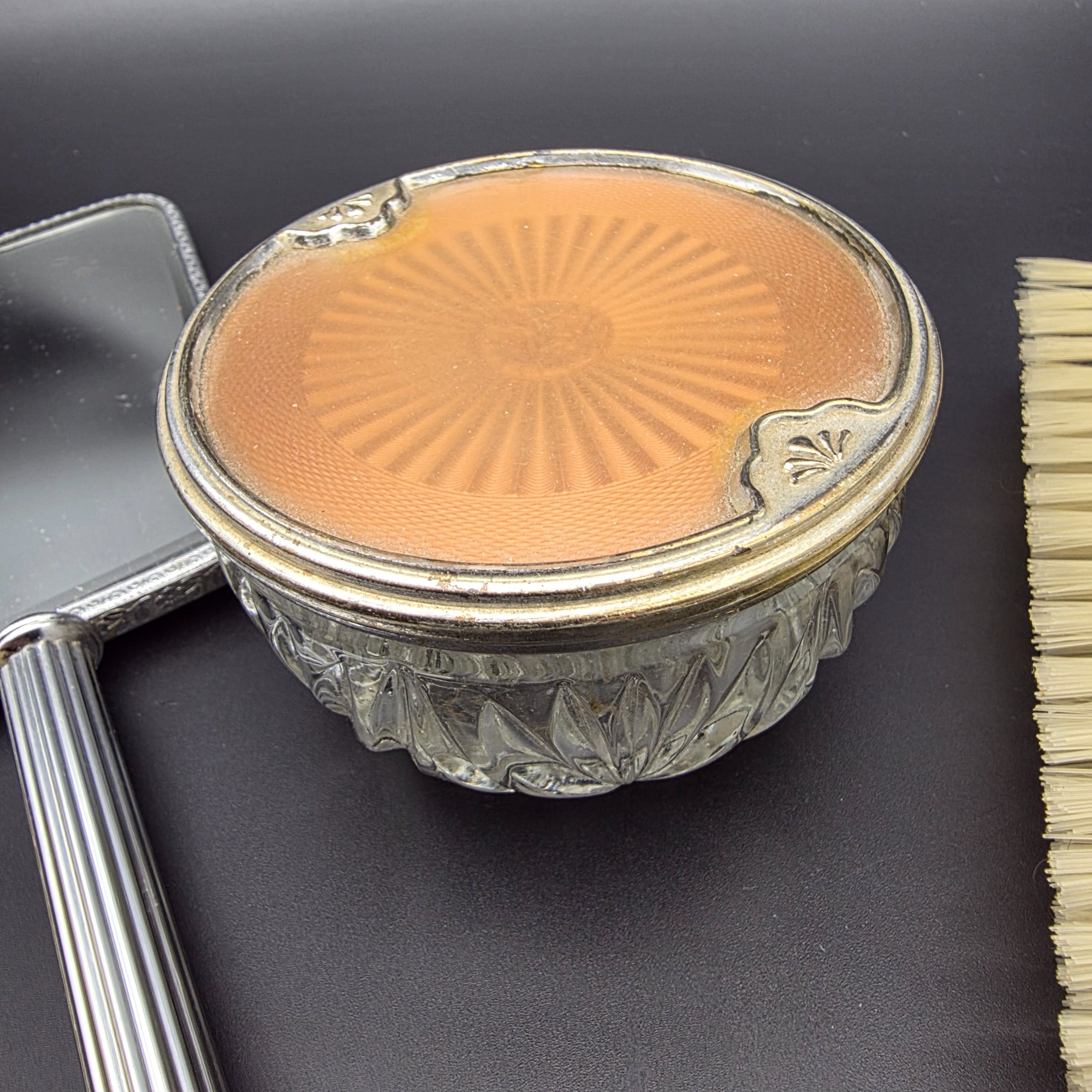 A five-piece vintage Art Deco dressing table vanity set, featuring a hand mirror, two brushes, and a lidded glass powder jar, all with silver-tone metal and rose-gold toned celluloid fan-patterned inserts. - View 3