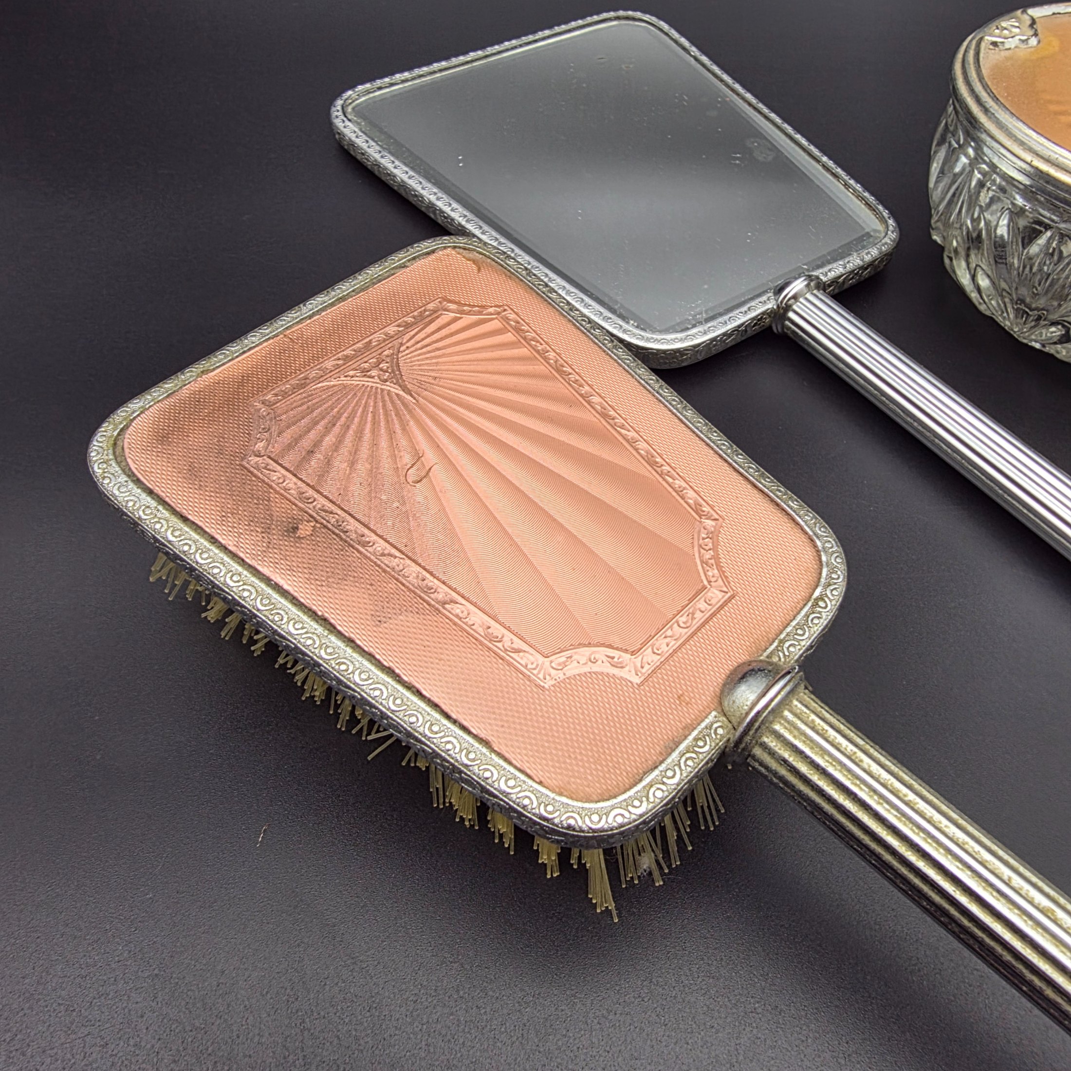 A five-piece vintage Art Deco dressing table vanity set, featuring a hand mirror, two brushes, and a lidded glass powder jar, all with silver-tone metal and rose-gold toned celluloid fan-patterned inserts. - View 5