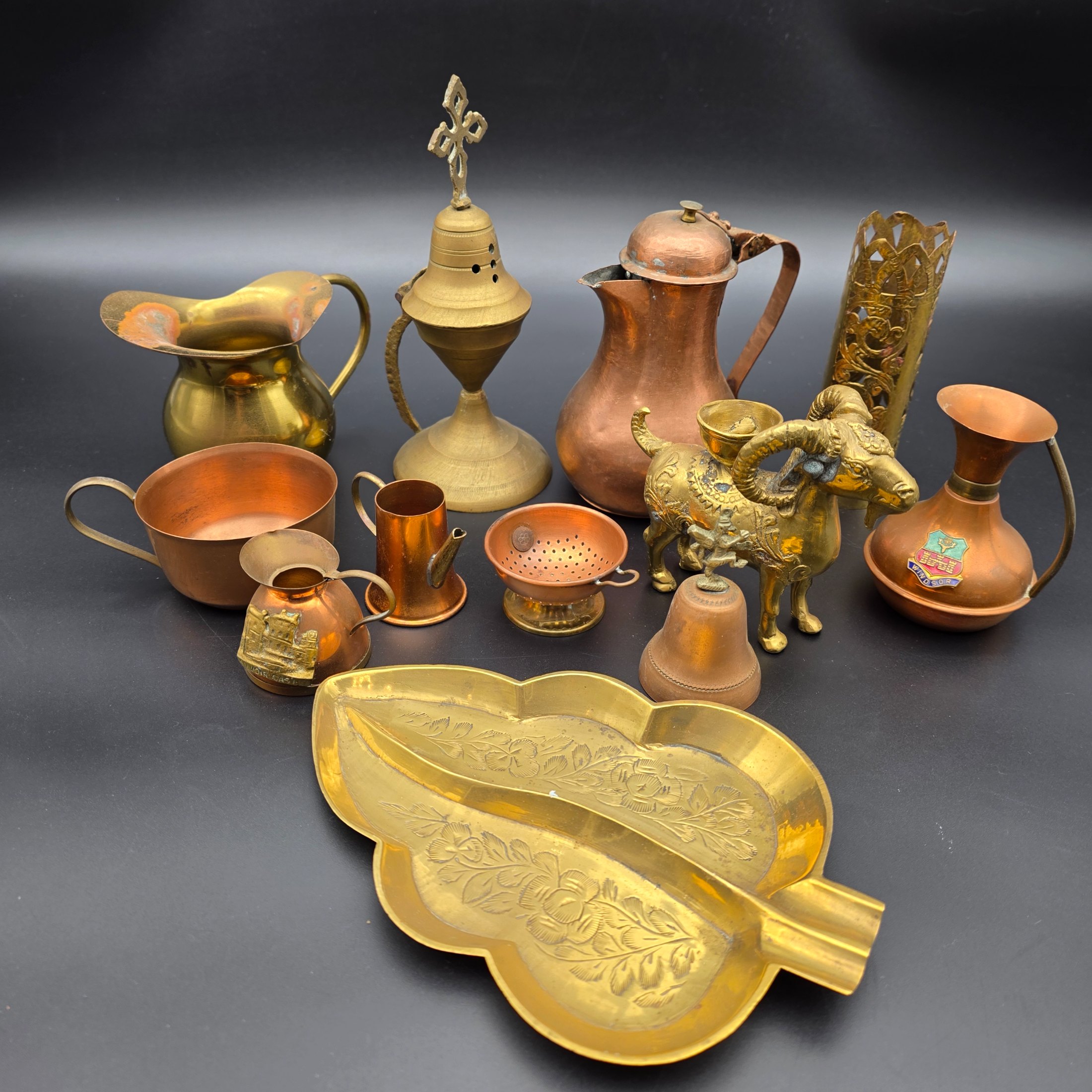 A diverse collection of antique and vintage decorative items, primarily crafted from brass and copper, showcasing various forms such as jugs, a censer, a figurine, and an ornate leaf-shaped dish.