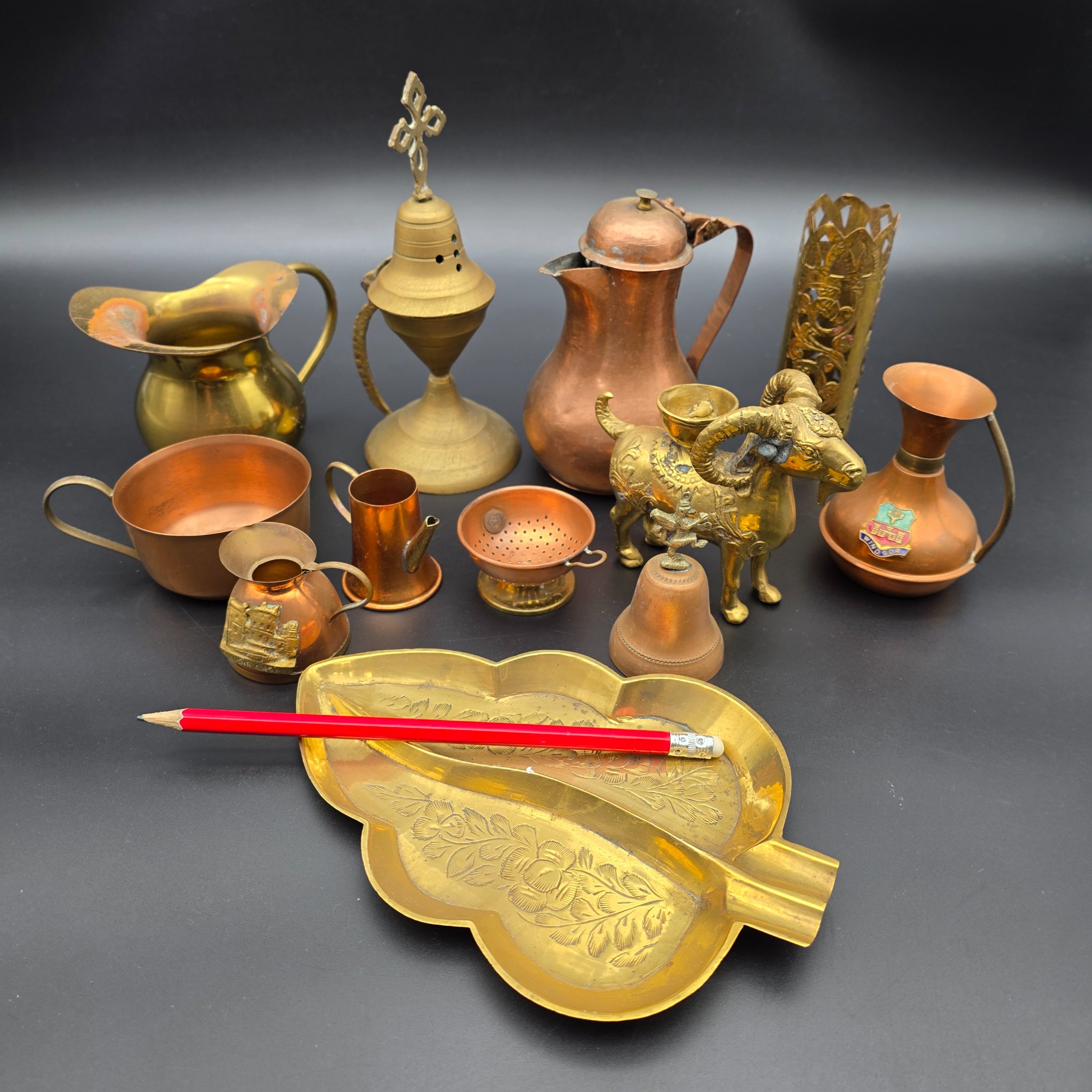 A diverse collection of antique and vintage decorative items, primarily crafted from brass and copper, showcasing various forms such as jugs, a censer, a figurine, and an ornate leaf-shaped dish. - View 2