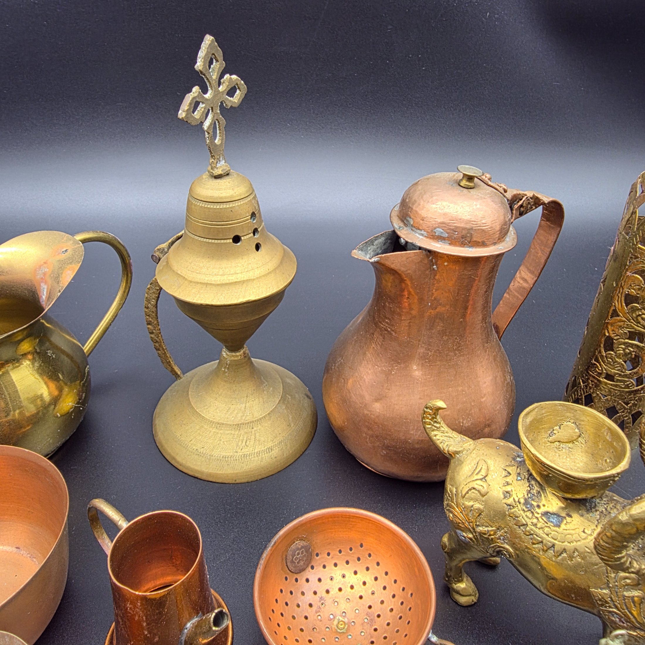 A diverse collection of antique and vintage decorative items, primarily crafted from brass and copper, showcasing various forms such as jugs, a censer, a figurine, and an ornate leaf-shaped dish. - View 4