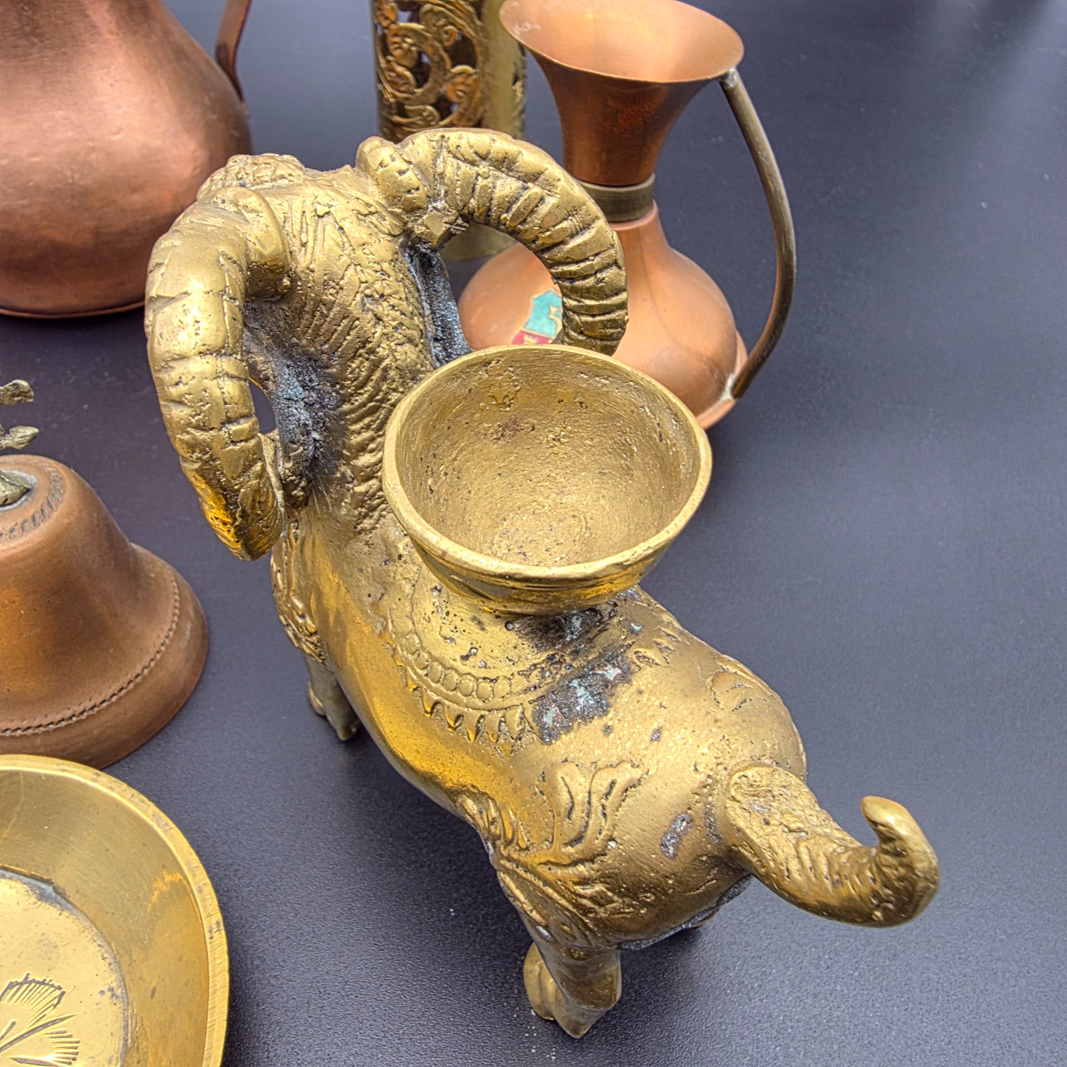 A diverse collection of antique and vintage decorative items, primarily crafted from brass and copper, showcasing various forms such as jugs, a censer, a figurine, and an ornate leaf-shaped dish. - View 6