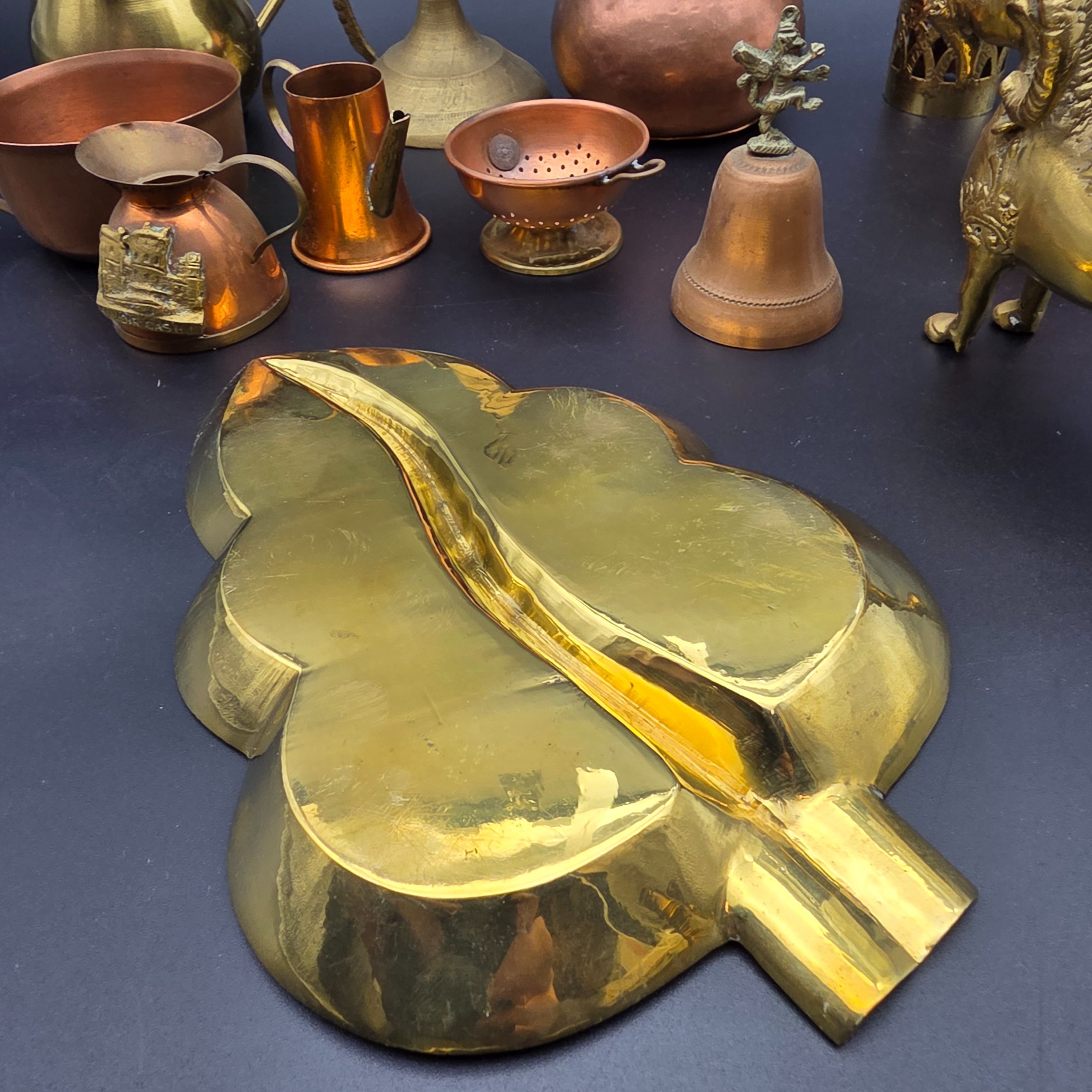 A diverse collection of antique and vintage decorative items, primarily crafted from brass and copper, showcasing various forms such as jugs, a censer, a figurine, and an ornate leaf-shaped dish. - View 7