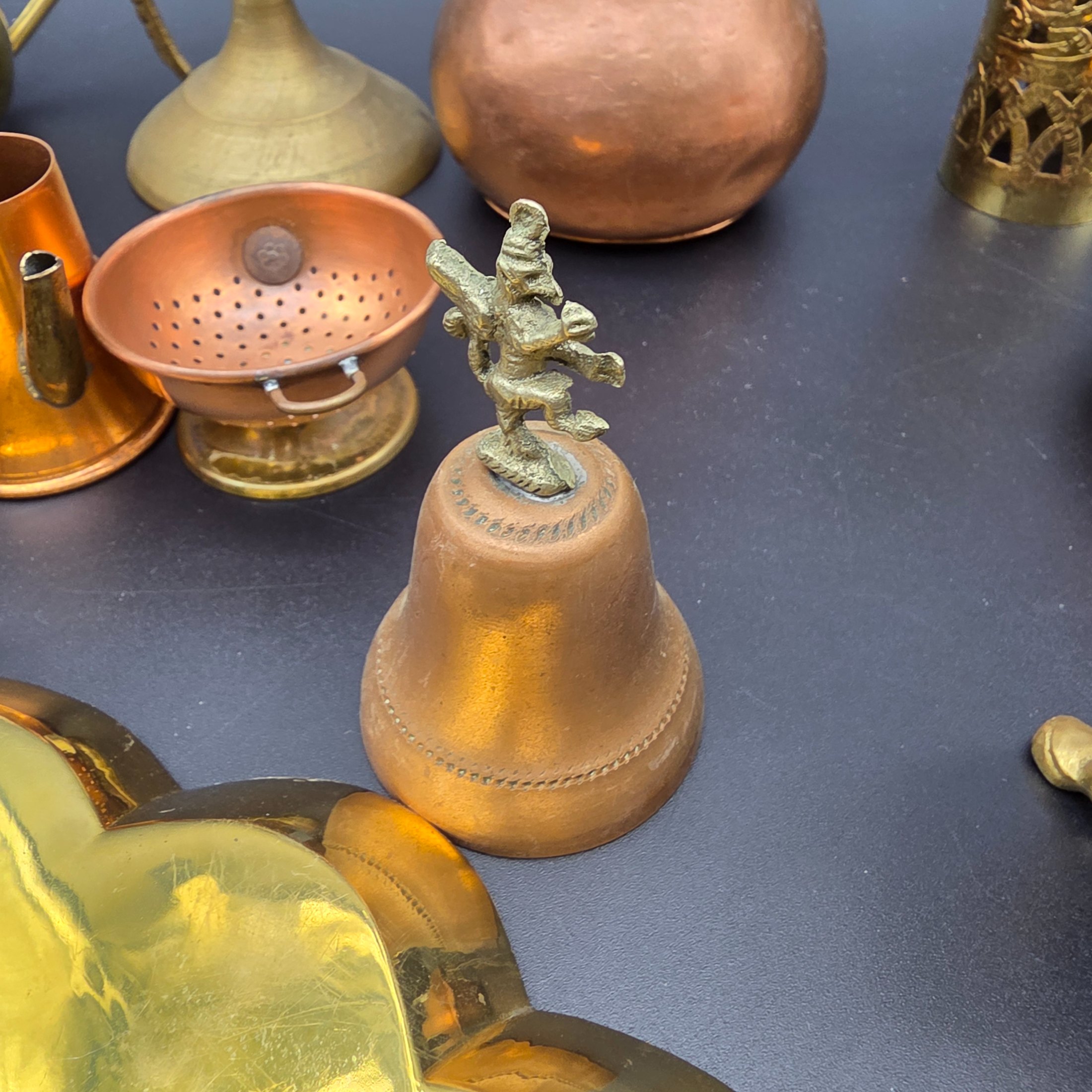 A diverse collection of antique and vintage decorative items, primarily crafted from brass and copper, showcasing various forms such as jugs, a censer, a figurine, and an ornate leaf-shaped dish. - View 8
