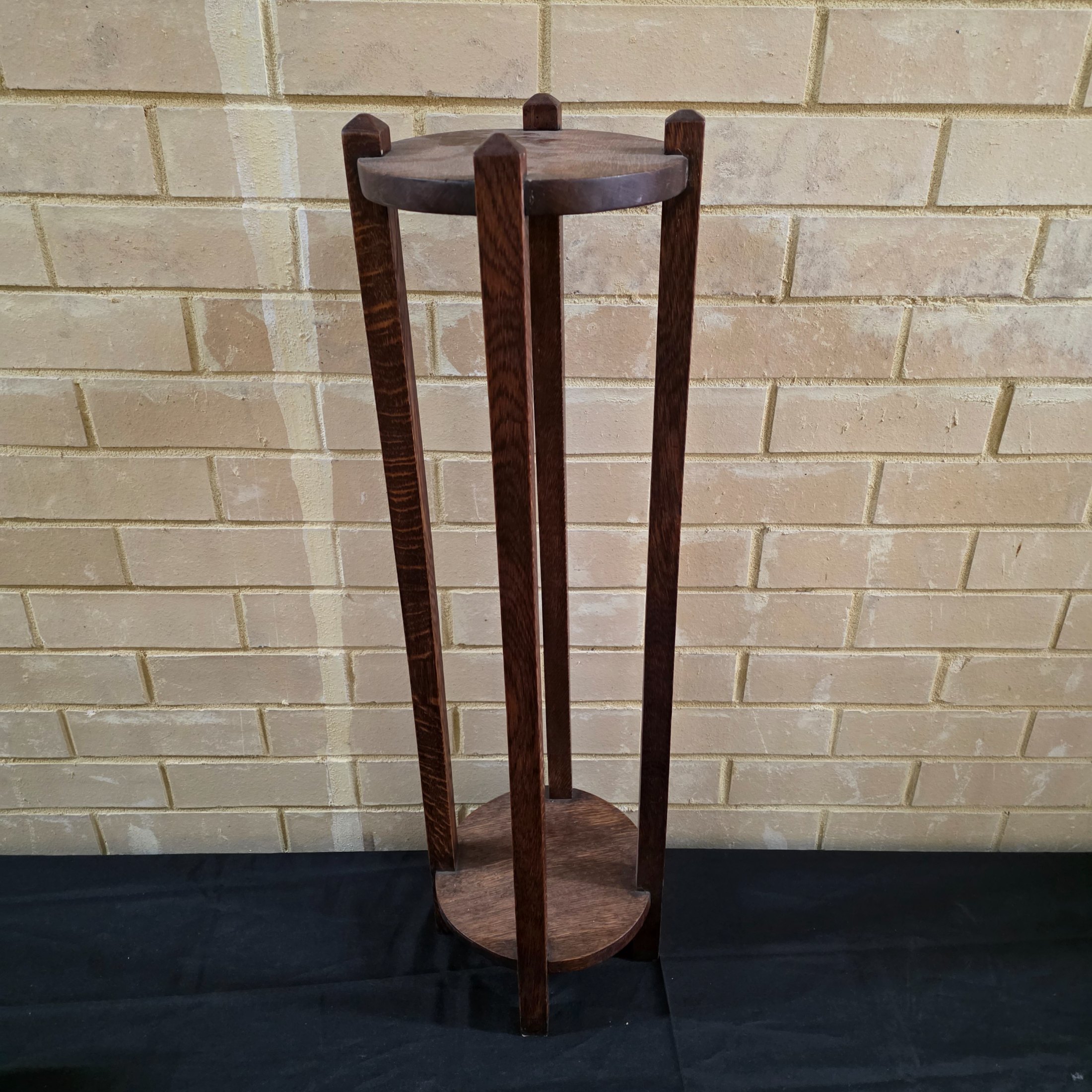 An Arts & Crafts dark oak plant stand or pedestal with a circular top and base, circa early 20th century.