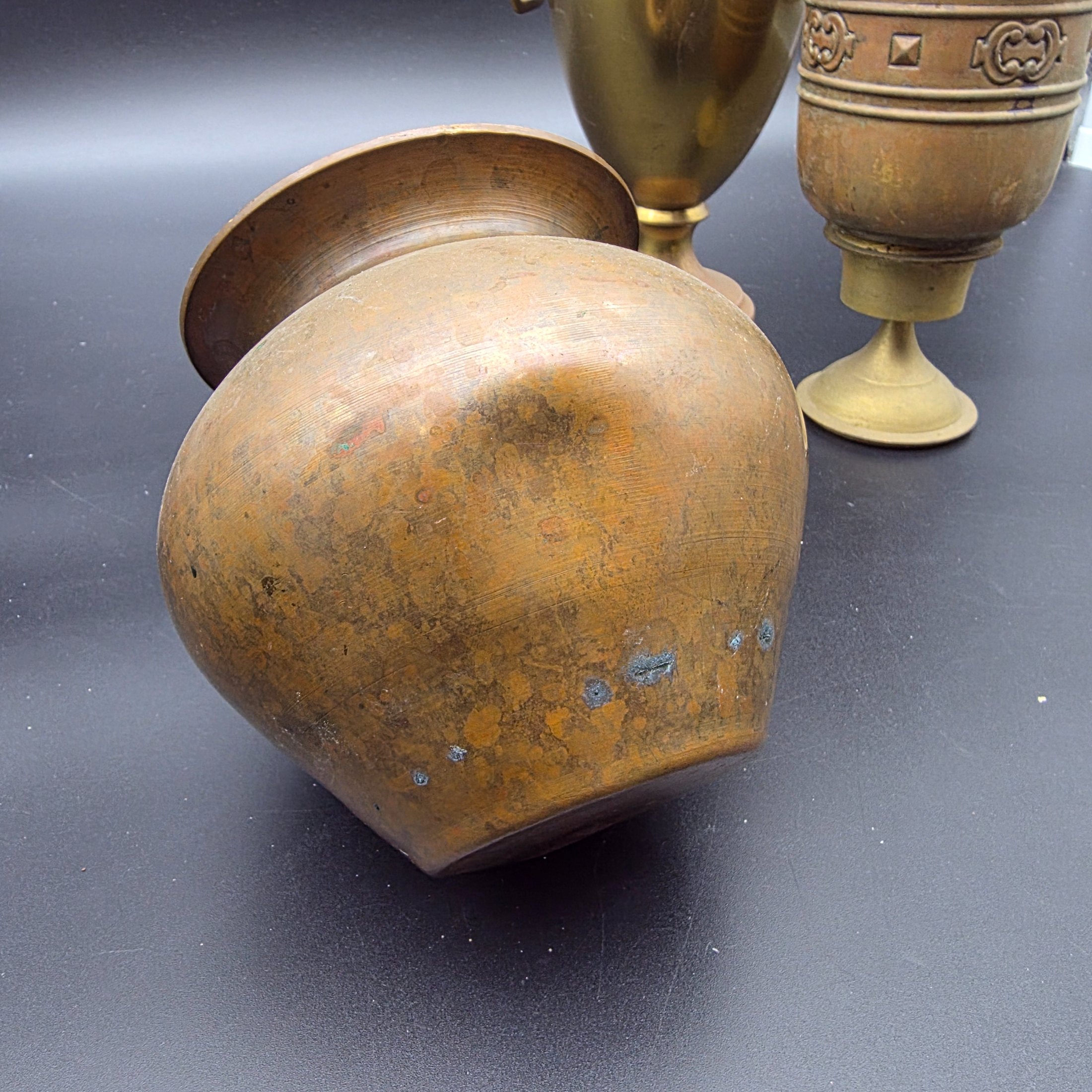 A varied collection of five vintage decorative vessels crafted from brass and copper, including a small footed goblet, a rounded copper pot, a brass bucket with a handle, a tall handled brass urn, and a footed brass goblet with ornate banding. At least one piece bears a 'MADE IN INDIA' label, indicating a probable origin for the entire group. - View 7