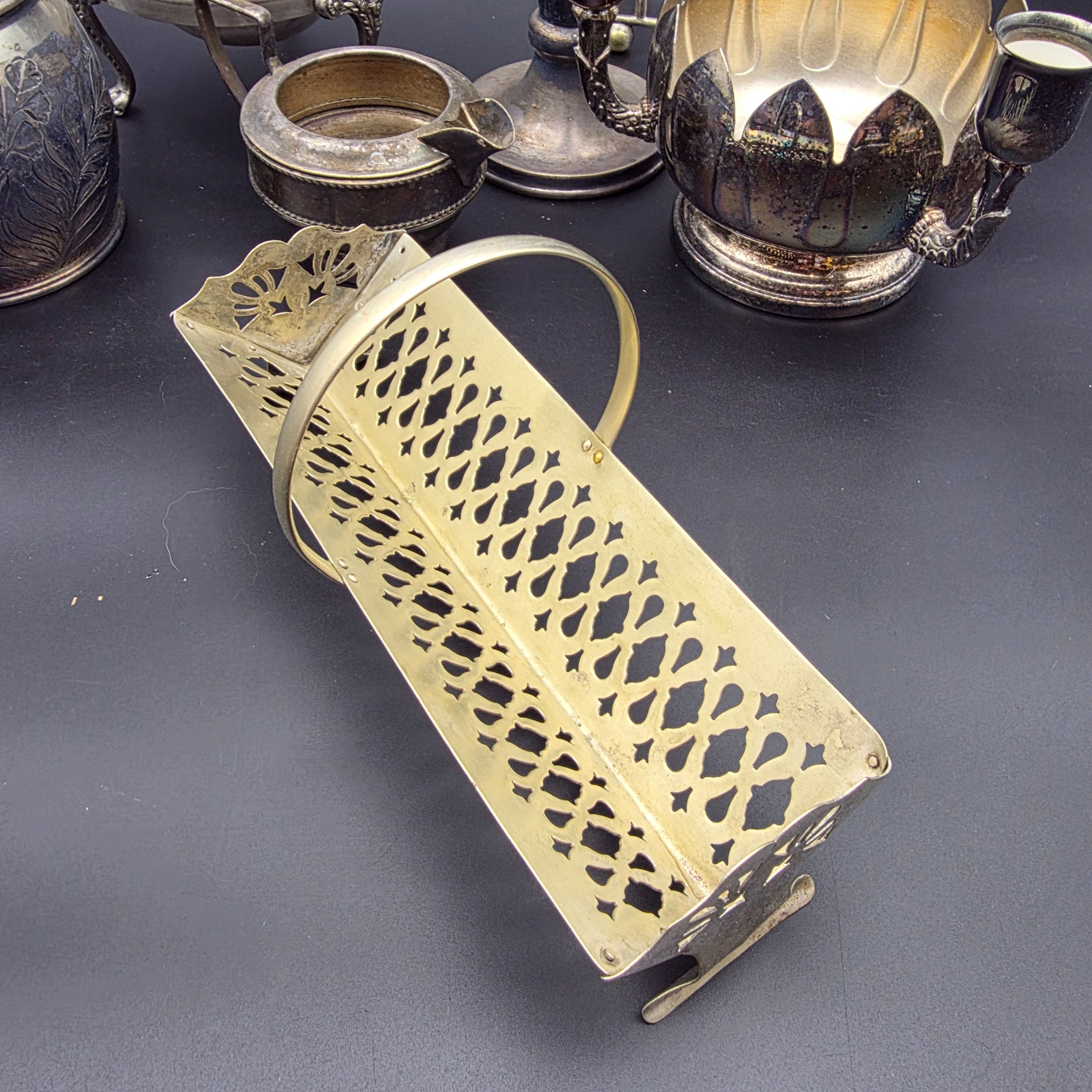 A varied collection of vintage silver-plated items including a butter dish, vase, creamer, bowls, and a toast rack, showing signs of heavy tarnishing and wear. - View 2