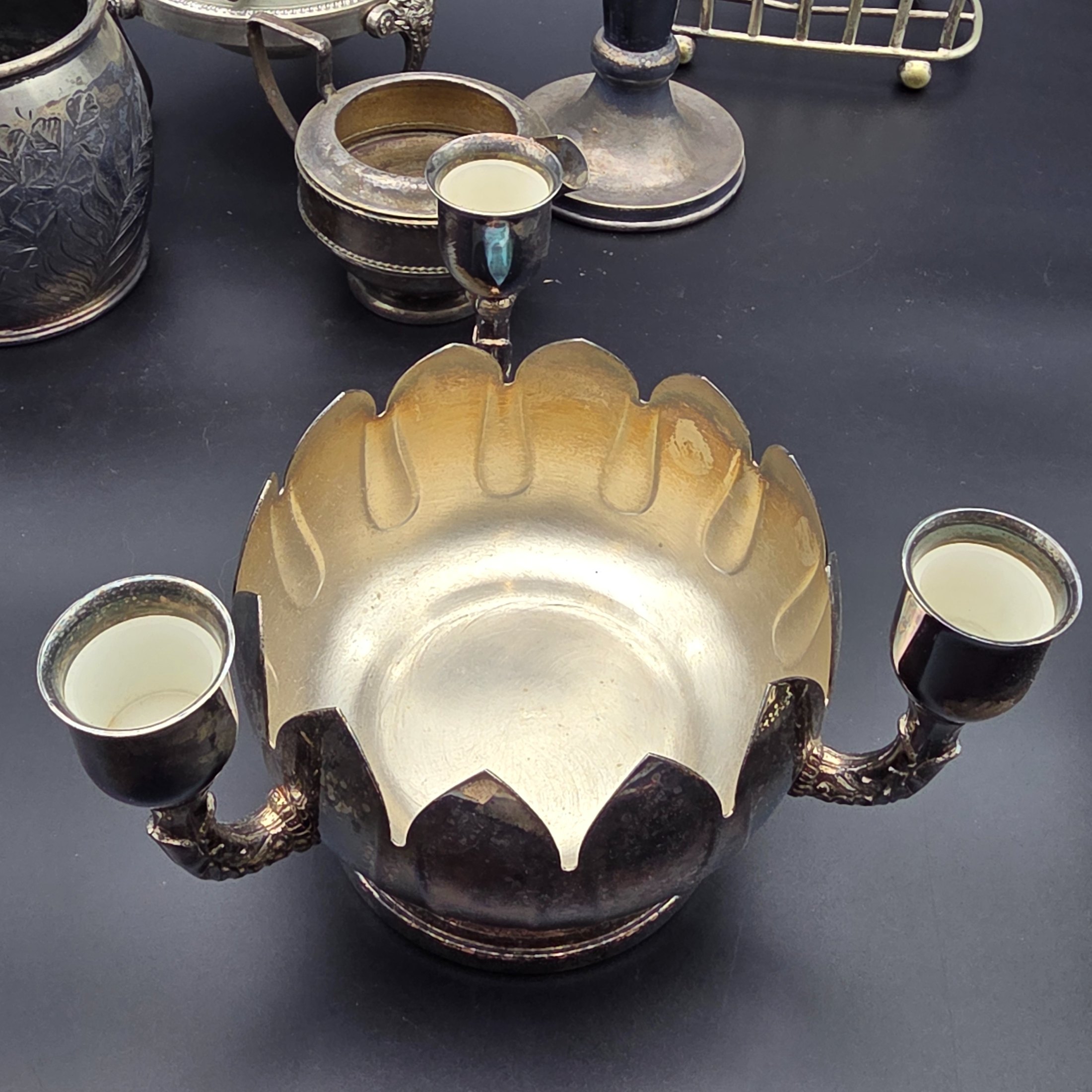 A varied collection of vintage silver-plated items including a butter dish, vase, creamer, bowls, and a toast rack, showing signs of heavy tarnishing and wear. - View 4