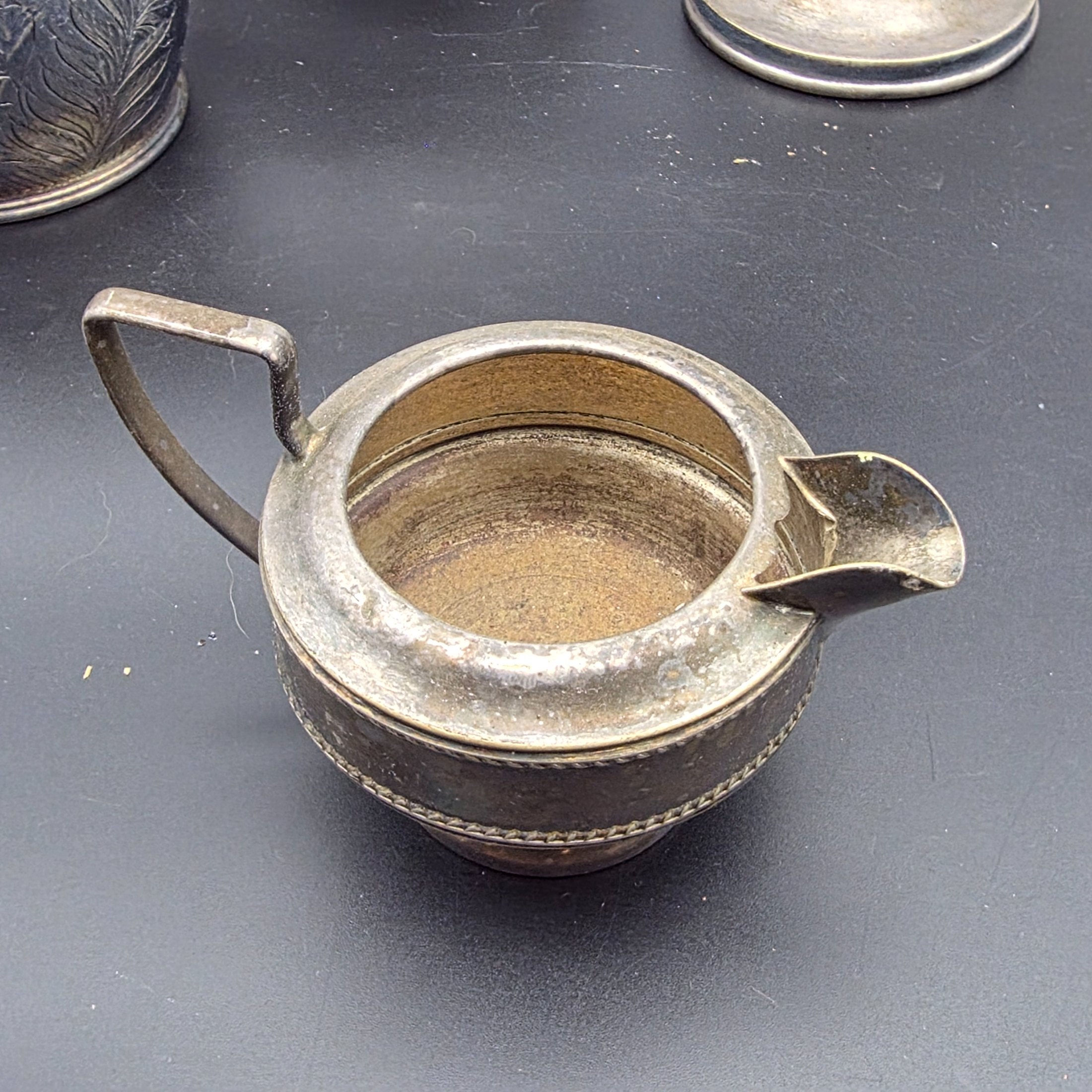 A varied collection of vintage silver-plated items including a butter dish, vase, creamer, bowls, and a toast rack, showing signs of heavy tarnishing and wear. - View 7