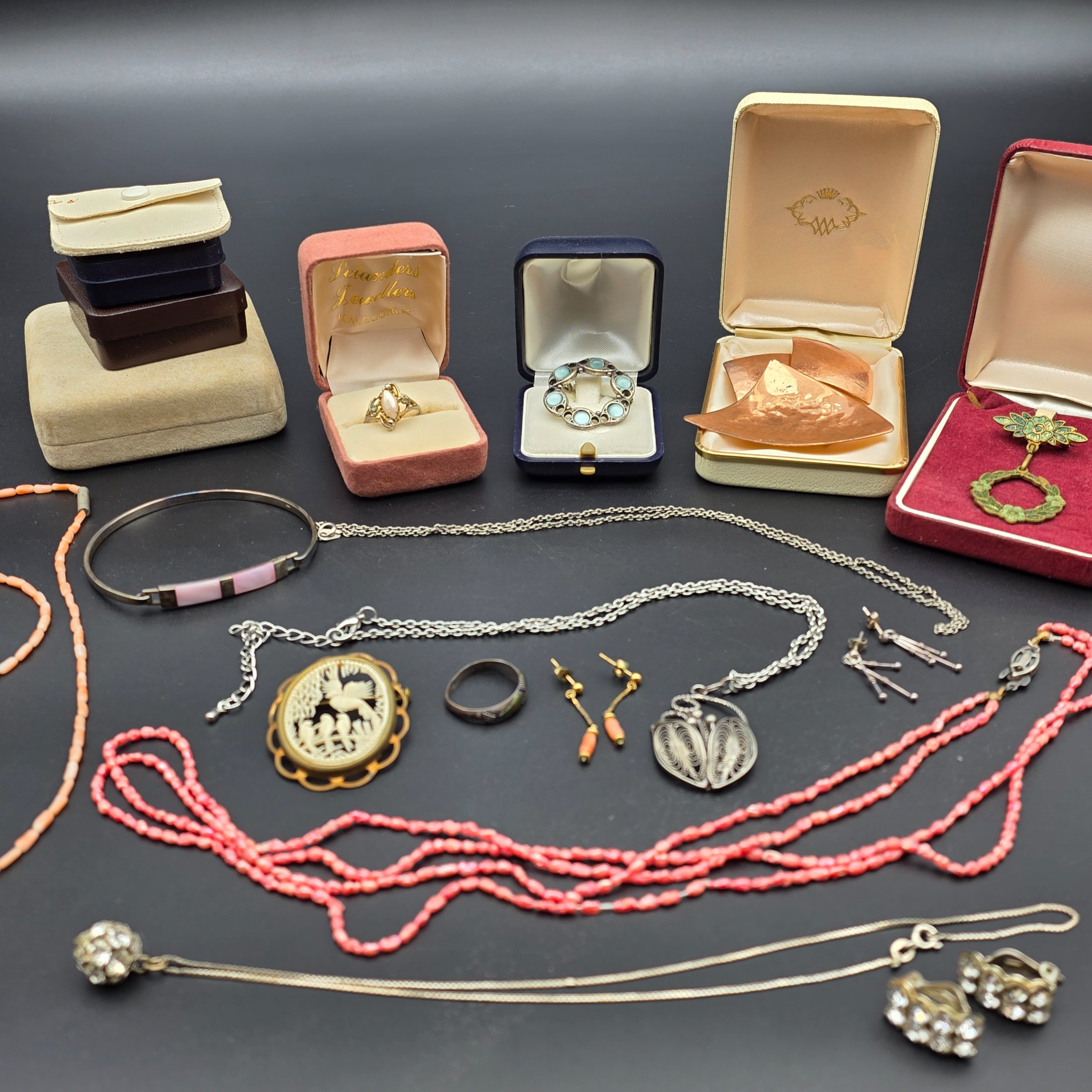 A diverse collection of vintage and sterling silver jewellery, including rings, brooches, necklaces, earrings, and a bangle, displayed across a dark surface.