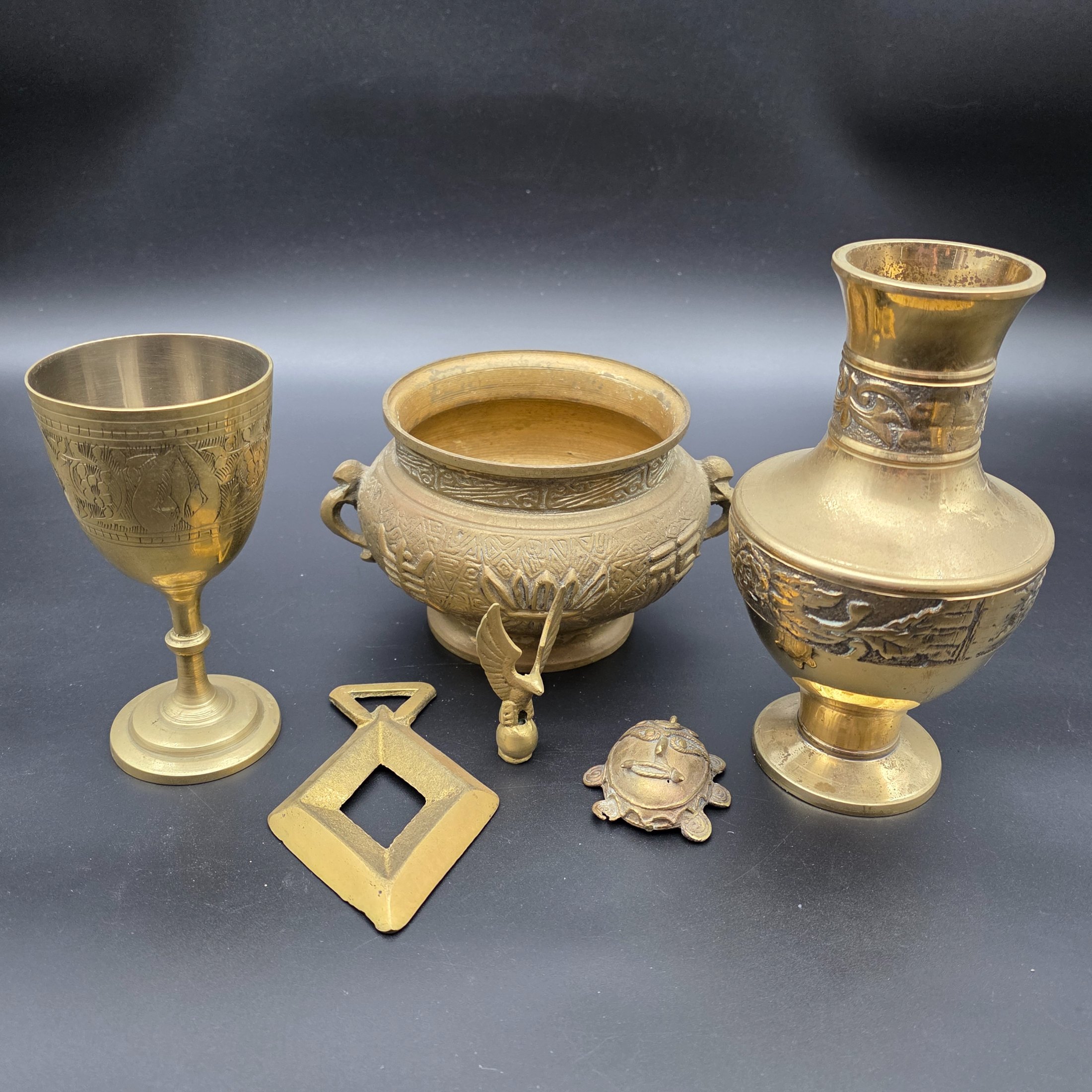 A collection of five assorted vintage brass ornamental pieces, including a goblet, vase, censer, and two smaller decorative items, all featuring intricate etchings and cast details.