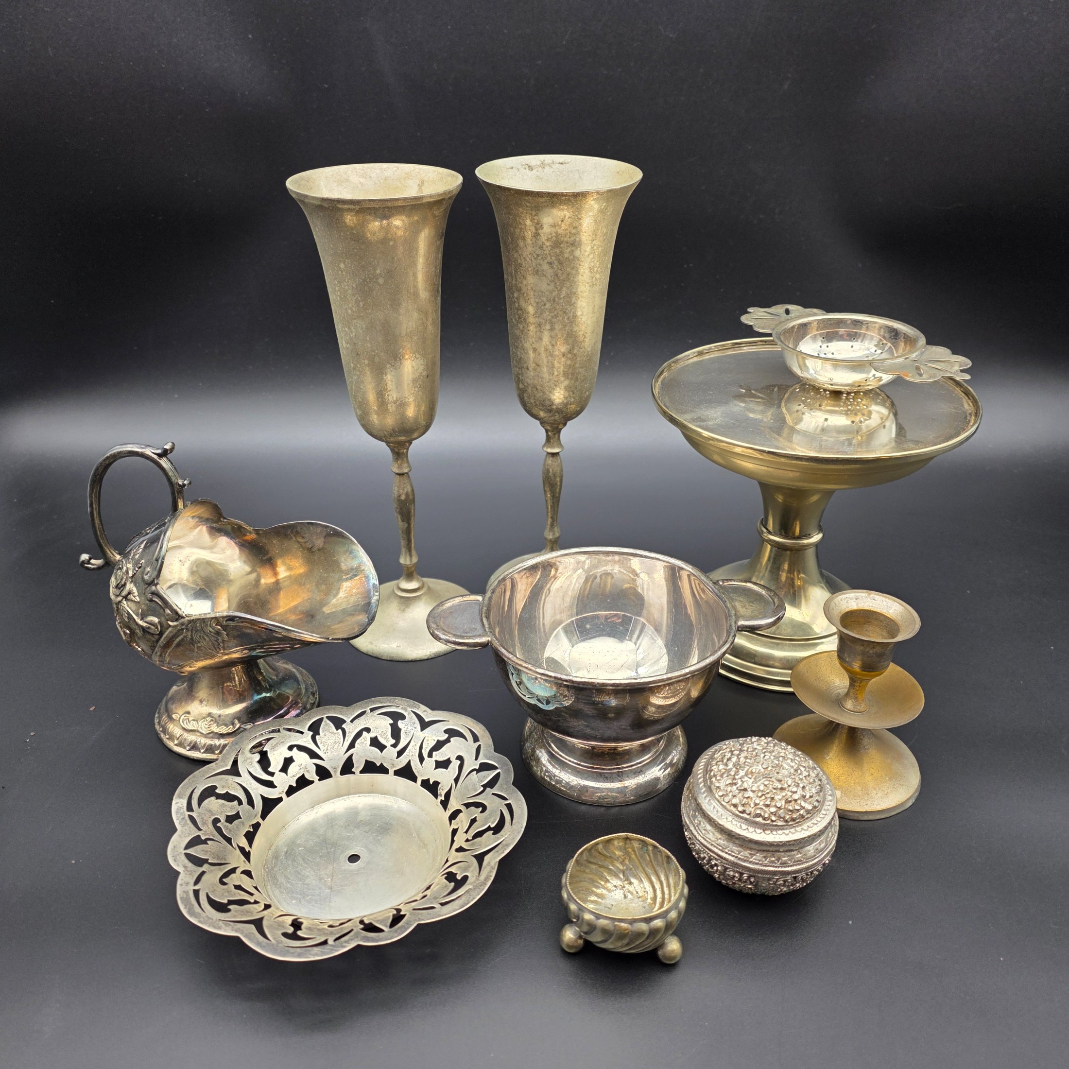 A diverse collection of antique and vintage metalware, primarily silver-plated and brass, featuring a variety of decorative and functional household items from the early to mid-20th century.