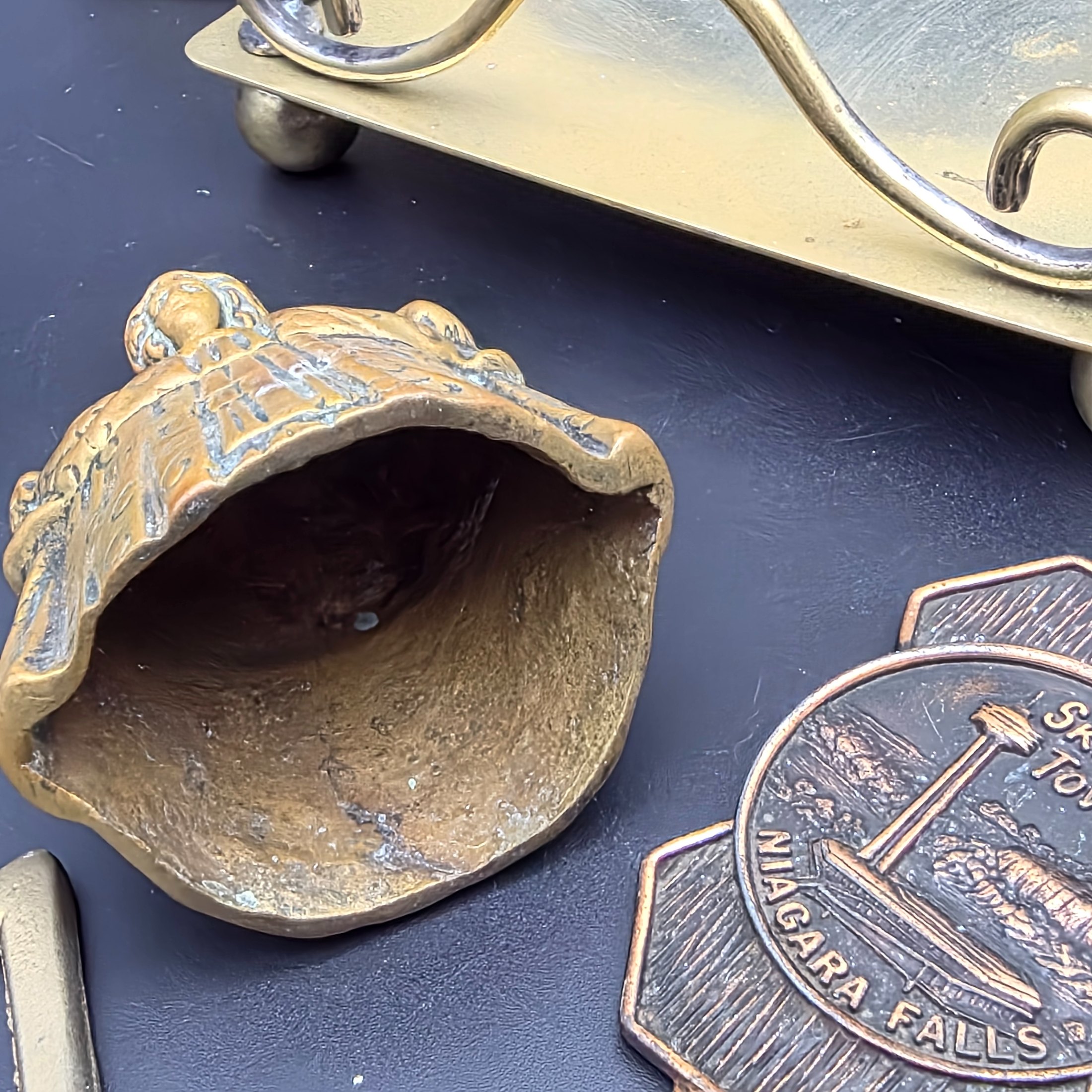A diverse collection of vintage decorative items crafted from brass and copper, including a tall vase, various ashtrays, a small handled tray, a bell, a letter opener, and other small metallic objects, likely from the mid-20th century. - View 5