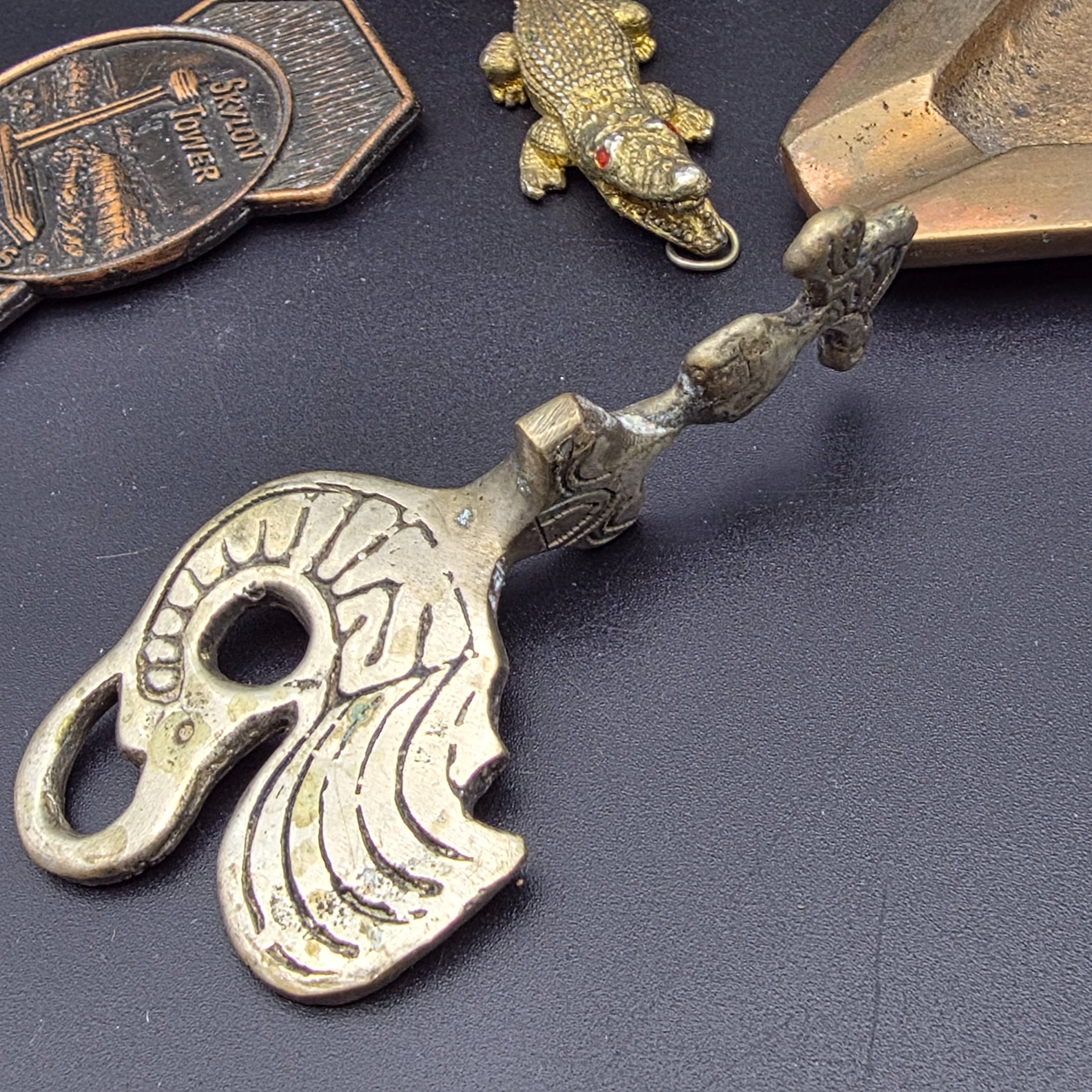 A diverse collection of vintage decorative items crafted from brass and copper, including a tall vase, various ashtrays, a small handled tray, a bell, a letter opener, and other small metallic objects, likely from the mid-20th century. - View 7