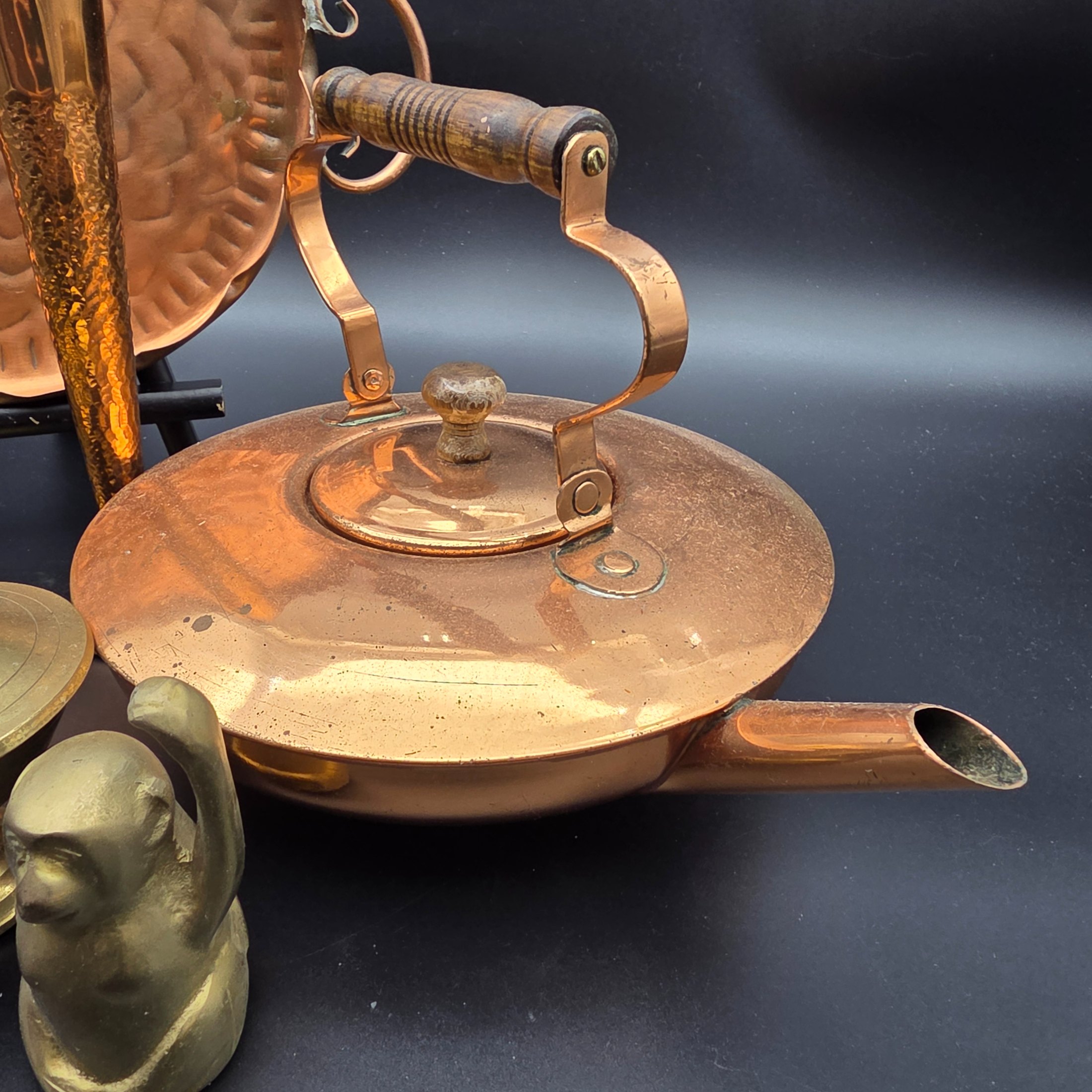 A collection of vintage copper and brass homewares, featuring a large decorative tray, a kettle, a candlestick, an ashtray, a lidded pot, a small vase, and a monkey bell. - View 2