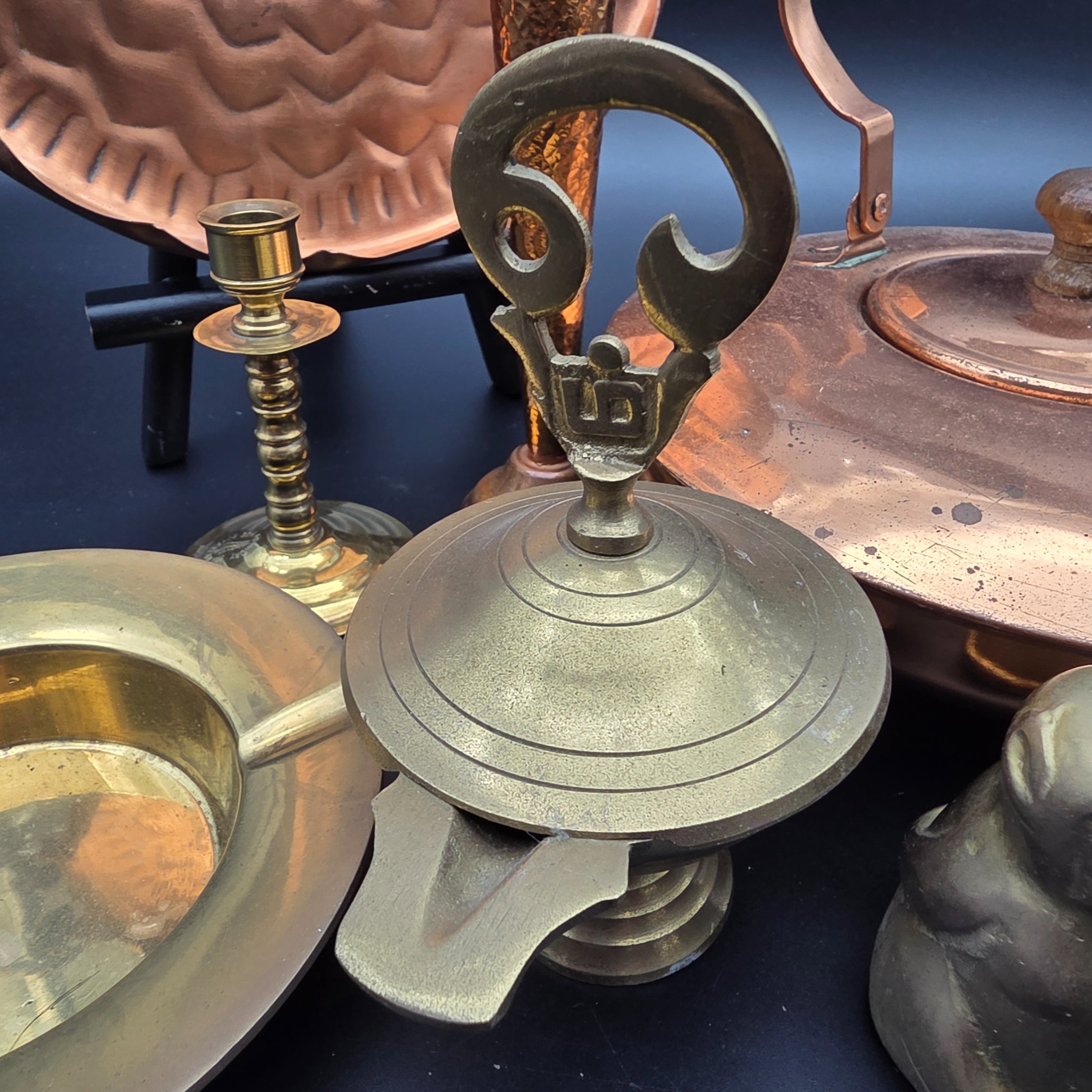 A collection of vintage copper and brass homewares, featuring a large decorative tray, a kettle, a candlestick, an ashtray, a lidded pot, a small vase, and a monkey bell. - View 3