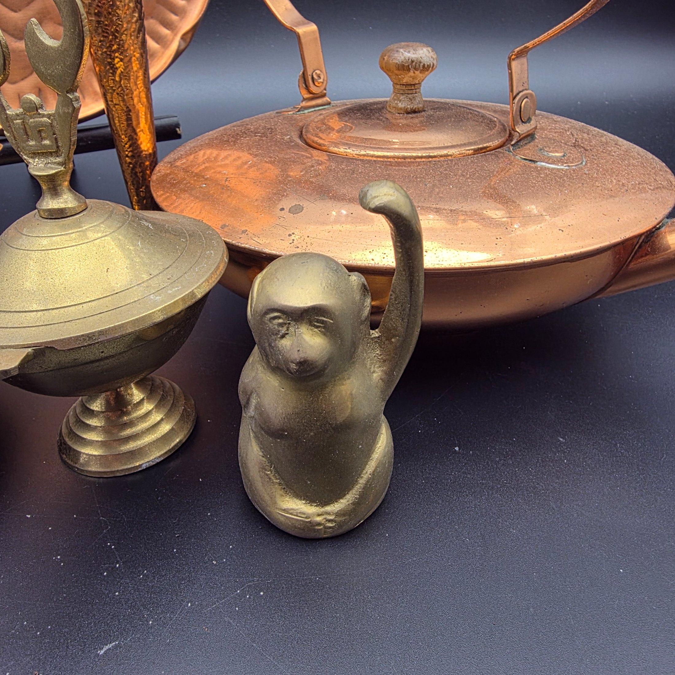 A collection of vintage copper and brass homewares, featuring a large decorative tray, a kettle, a candlestick, an ashtray, a lidded pot, a small vase, and a monkey bell. - View 4