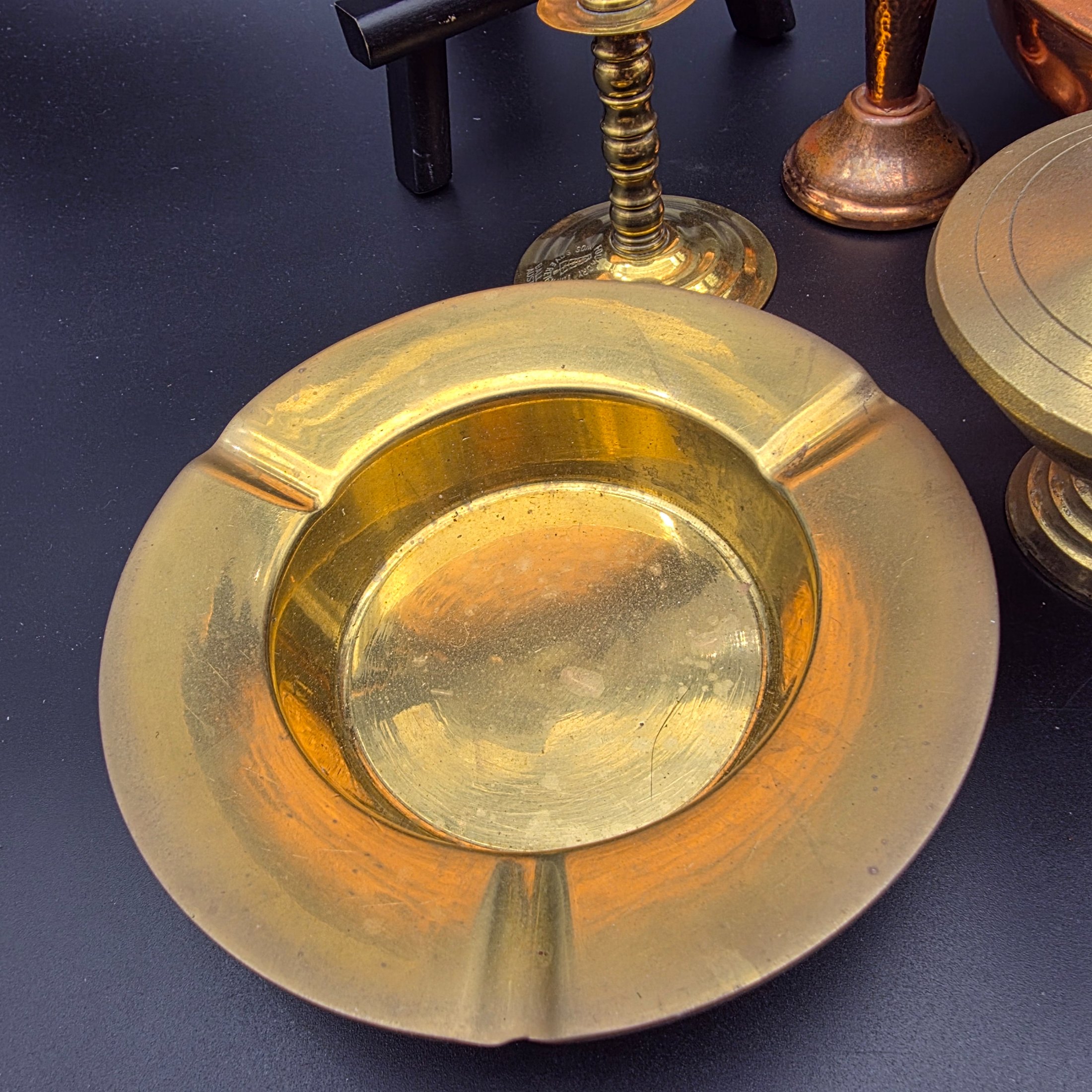 A collection of vintage copper and brass homewares, featuring a large decorative tray, a kettle, a candlestick, an ashtray, a lidded pot, a small vase, and a monkey bell. - View 5