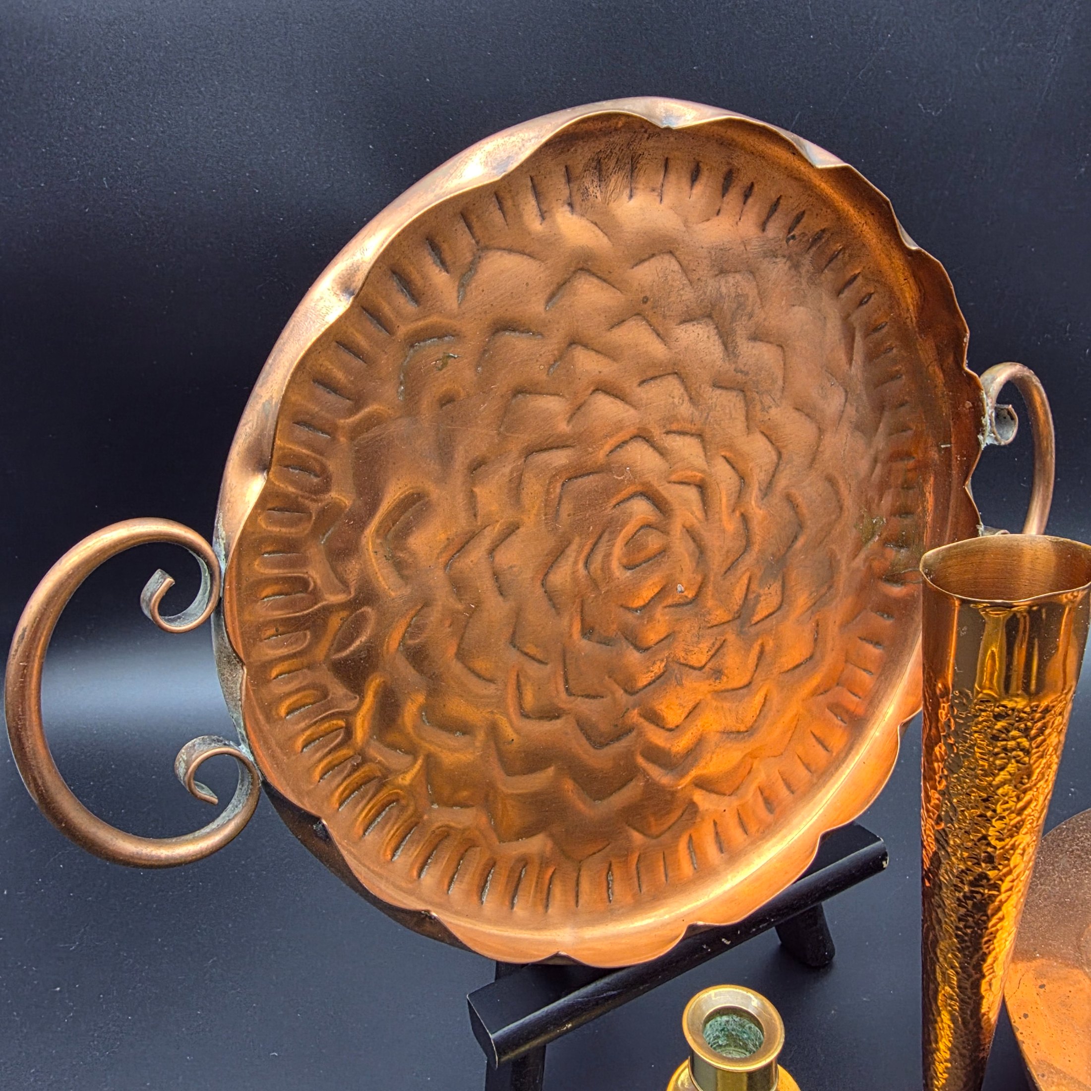 A collection of vintage copper and brass homewares, featuring a large decorative tray, a kettle, a candlestick, an ashtray, a lidded pot, a small vase, and a monkey bell. - View 6