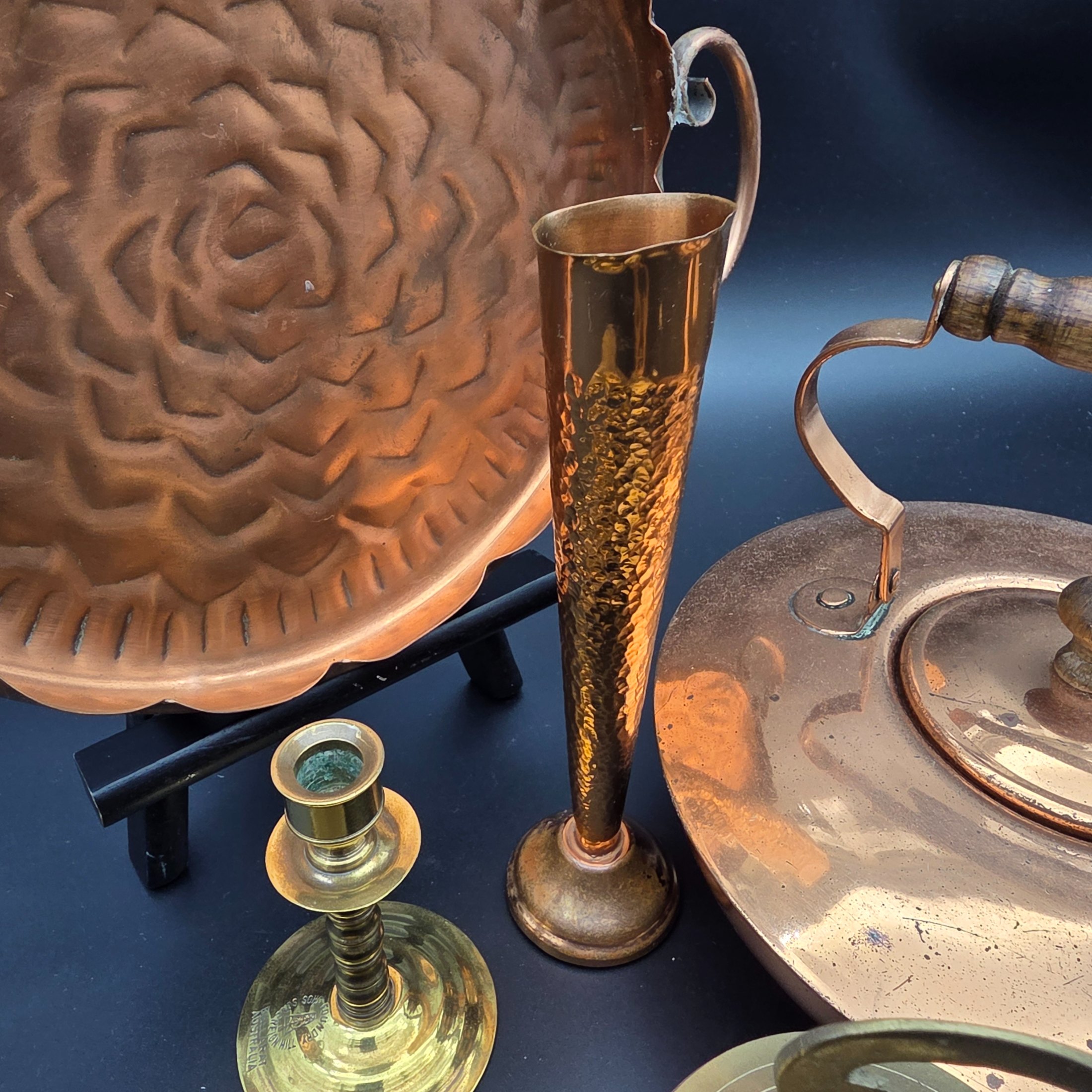 A collection of vintage copper and brass homewares, featuring a large decorative tray, a kettle, a candlestick, an ashtray, a lidded pot, a small vase, and a monkey bell. - View 7