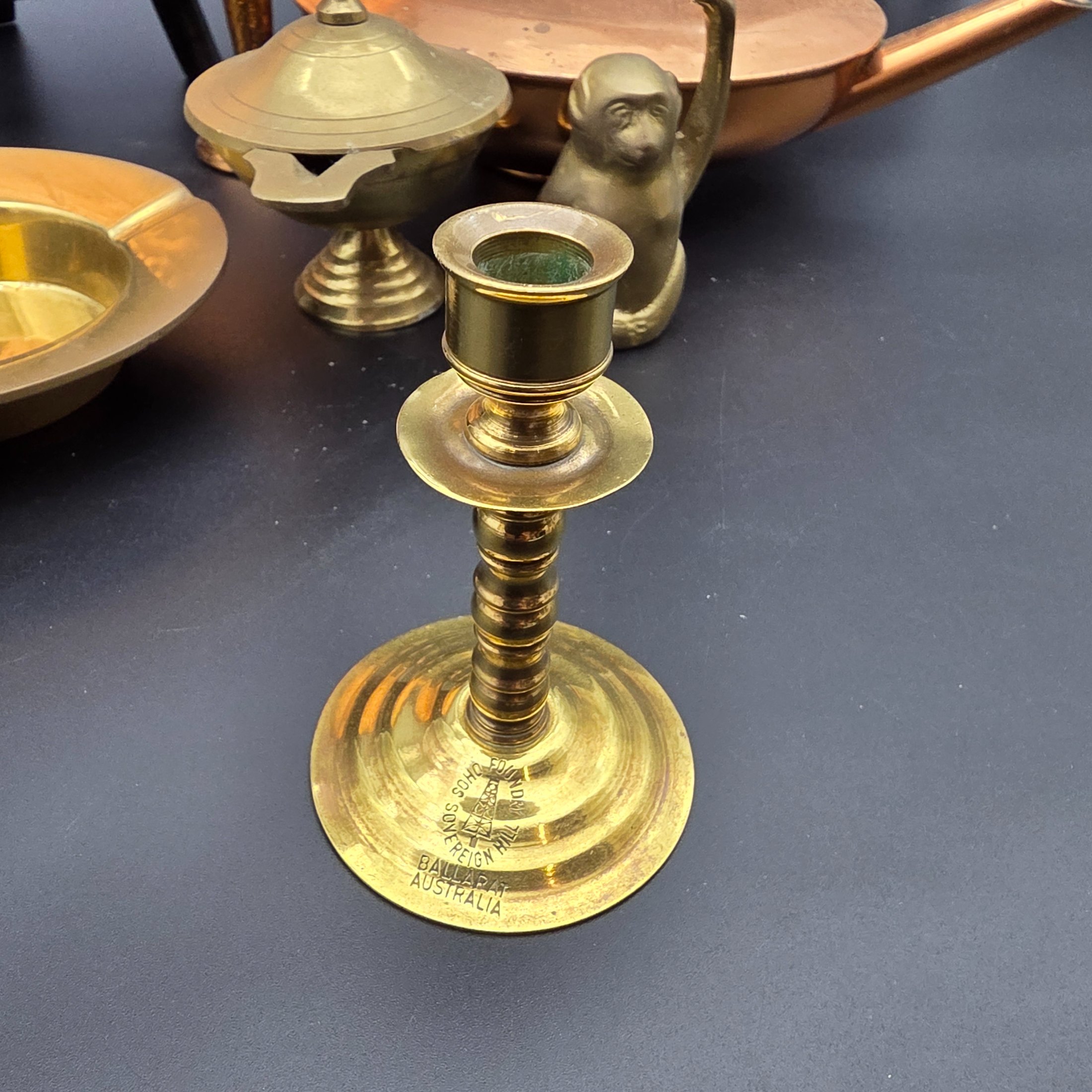 A collection of vintage copper and brass homewares, featuring a large decorative tray, a kettle, a candlestick, an ashtray, a lidded pot, a small vase, and a monkey bell. - View 8