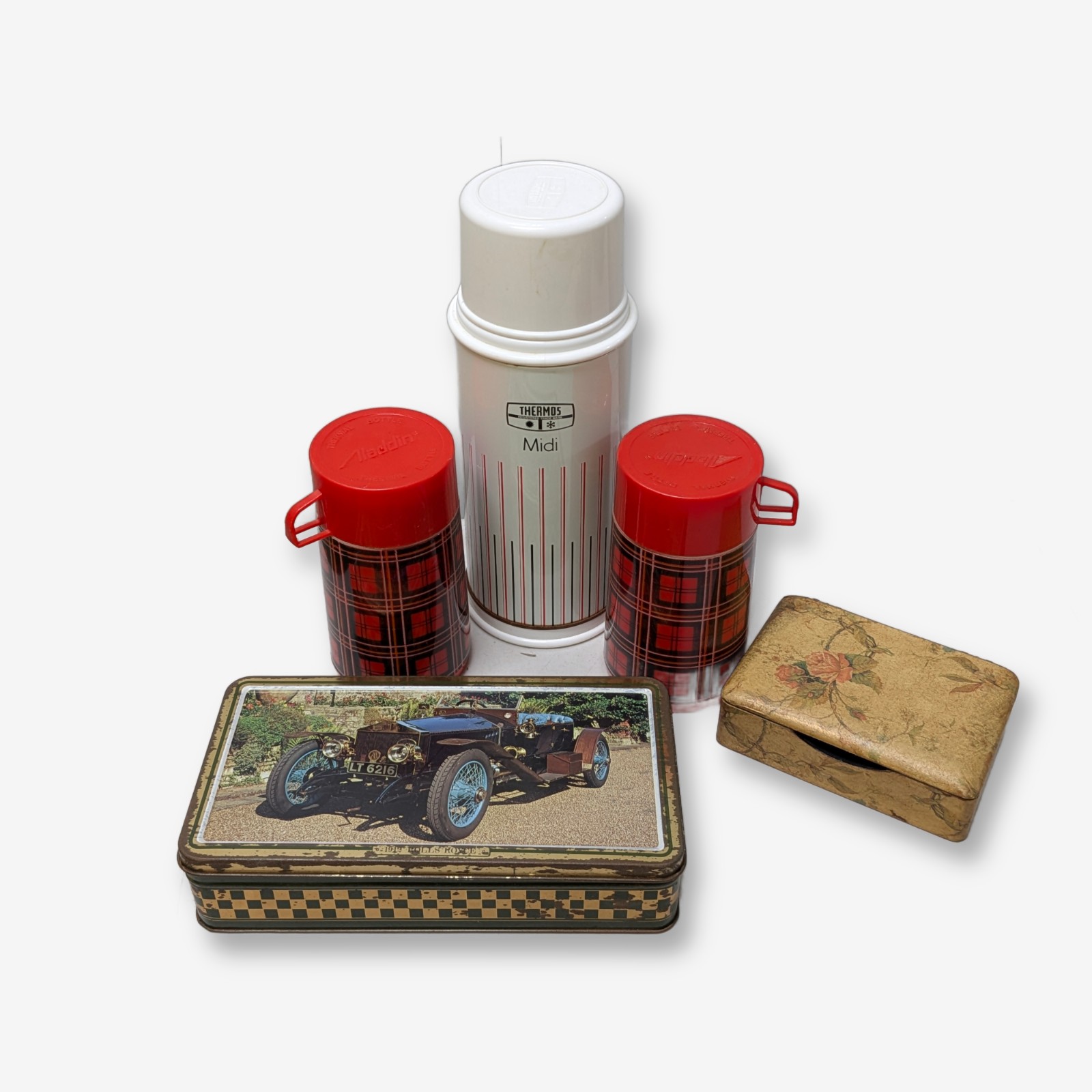 A charming collection of vintage homewares featuring a large white Thermos Midi flask, two smaller red plaid Aladdin thermal bottles, a rectangular metal tin adorned with a classic car image, and a small hinged wooden box with a floral motif.