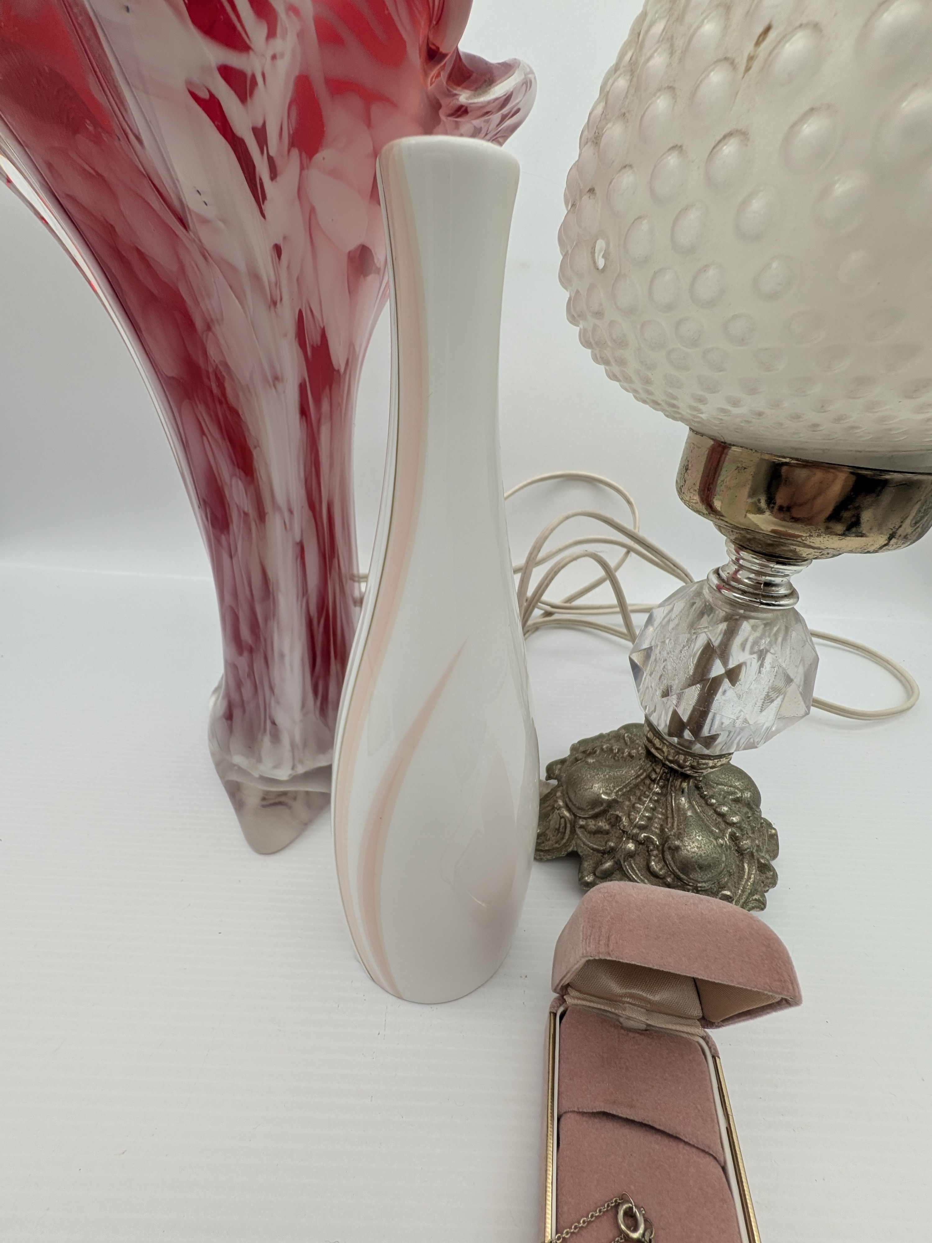 A charming collection of vintage decorative items, including a red art glass vase, a ceramic vase, a small hobnail glass table lamp, and a velvet jewellery box containing a silver-toned cameo necklace. - View 6
