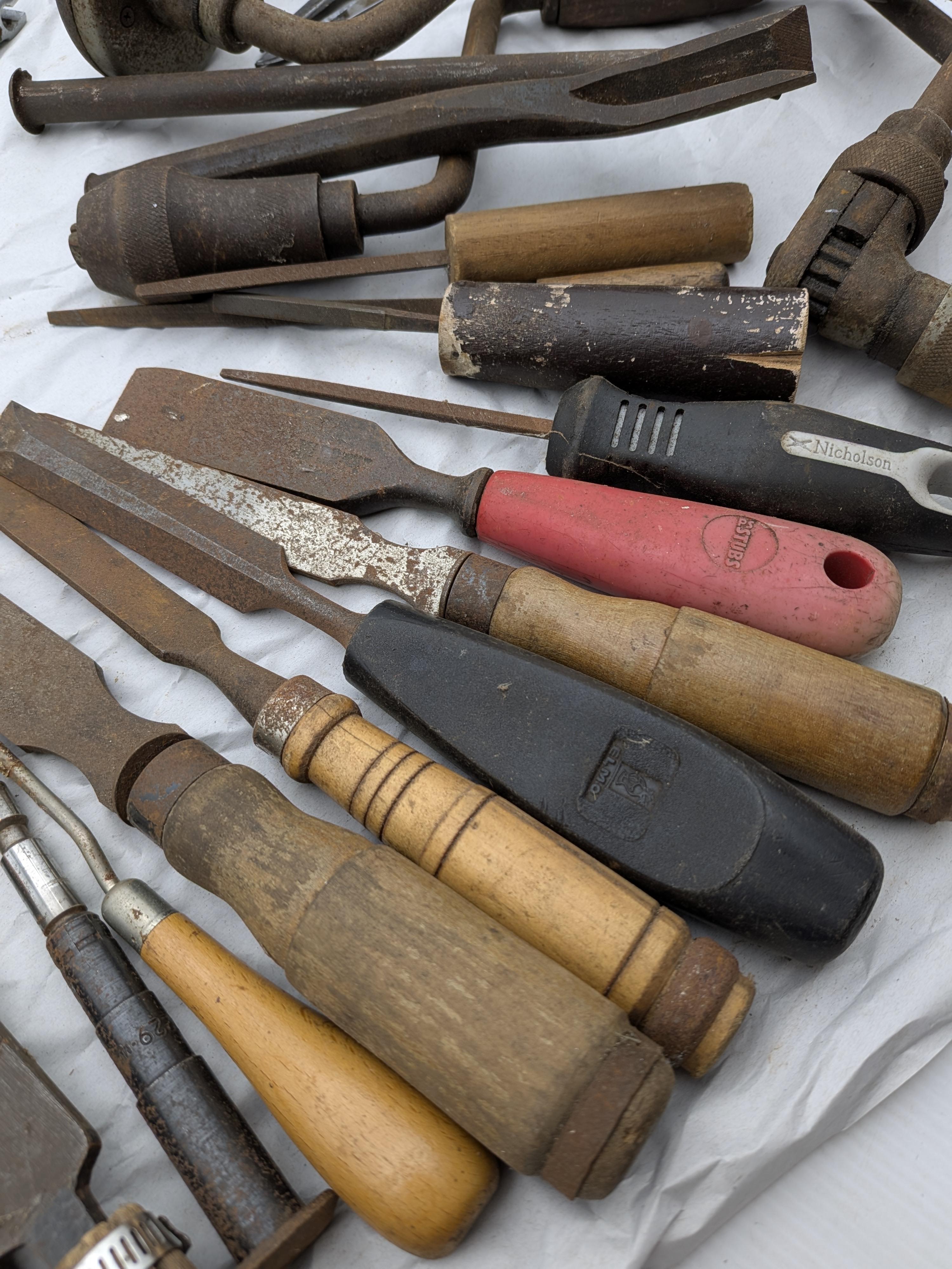 A large collection of assorted vintage hand tools, including various saws, files, chisels, wrenches, pliers, screwdrivers, and drills, exhibiting extensive surface rust and wear. - View 3