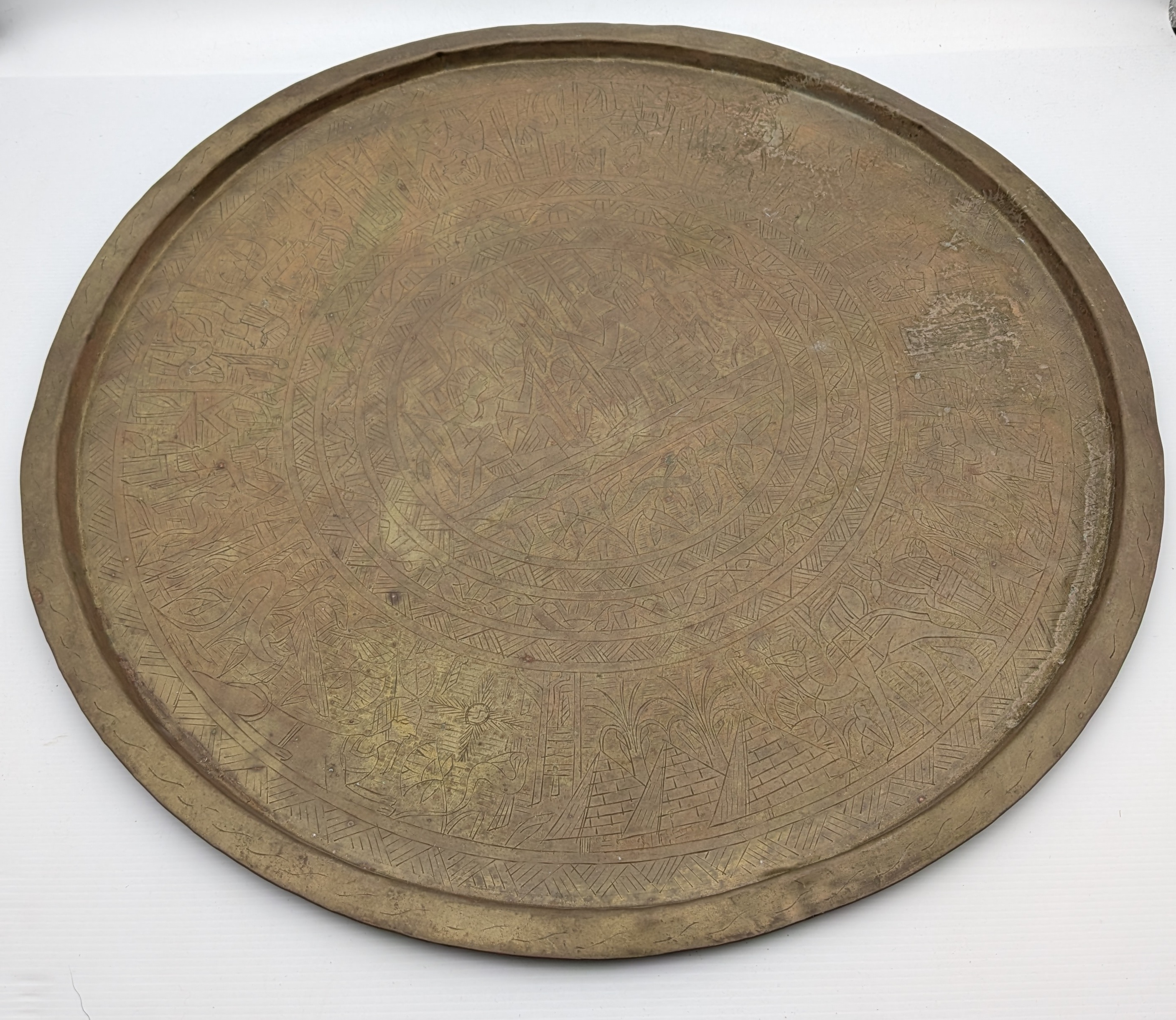 A substantial vintage etched brass tray, likely from the mid-20th century, showcasing traditional Middle Eastern or North African decorative metalwork. Its broad, circular form features intricate, deeply etched patterns across its surface, including figural elements, geometric motifs, and possibly calligraphic designs, characteristic of artisan craftsmanship from the region.