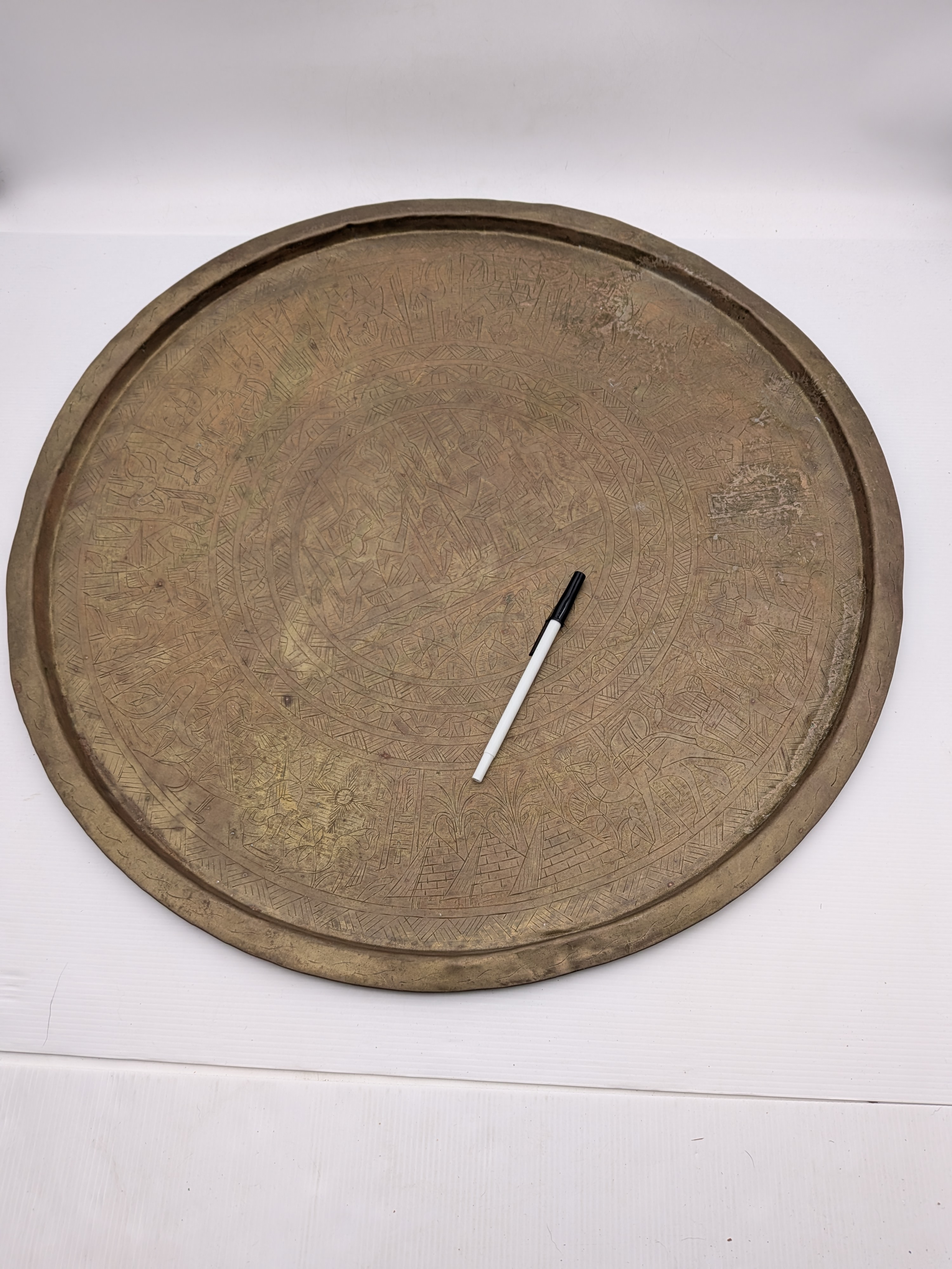 A substantial vintage etched brass tray, likely from the mid-20th century, showcasing traditional Middle Eastern or North African decorative metalwork. Its broad, circular form features intricate, deeply etched patterns across its surface, including figural elements, geometric motifs, and possibly calligraphic designs, characteristic of artisan craftsmanship from the region. - View 7