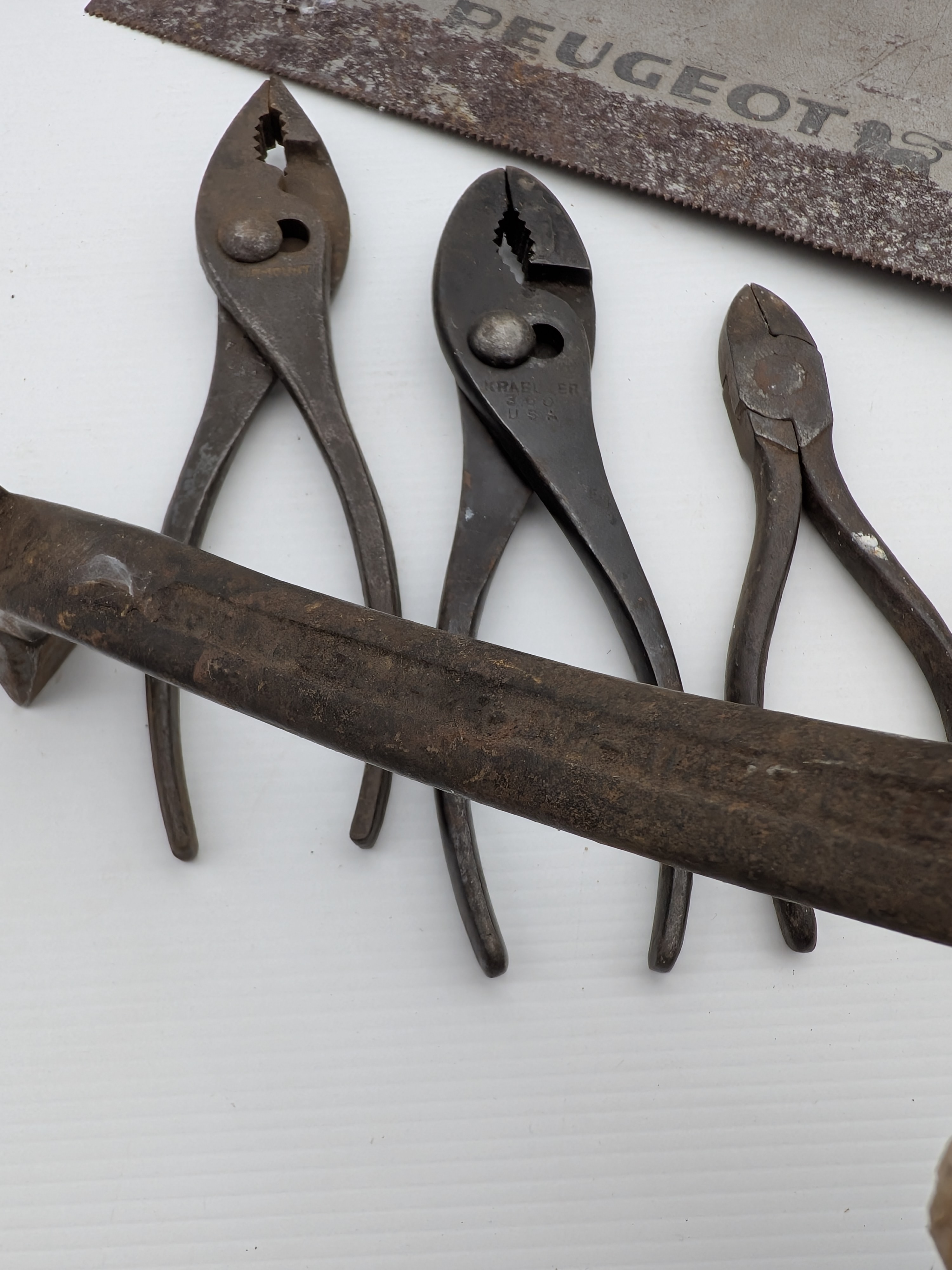 A comprehensive collection of vintage hand tools, including a Peugeot handsaw, assorted wrenches, pliers, pruning shears, horseshoes, and a bow saw frame, showcasing diverse forms and functions from the early to mid-20th century. - View 3