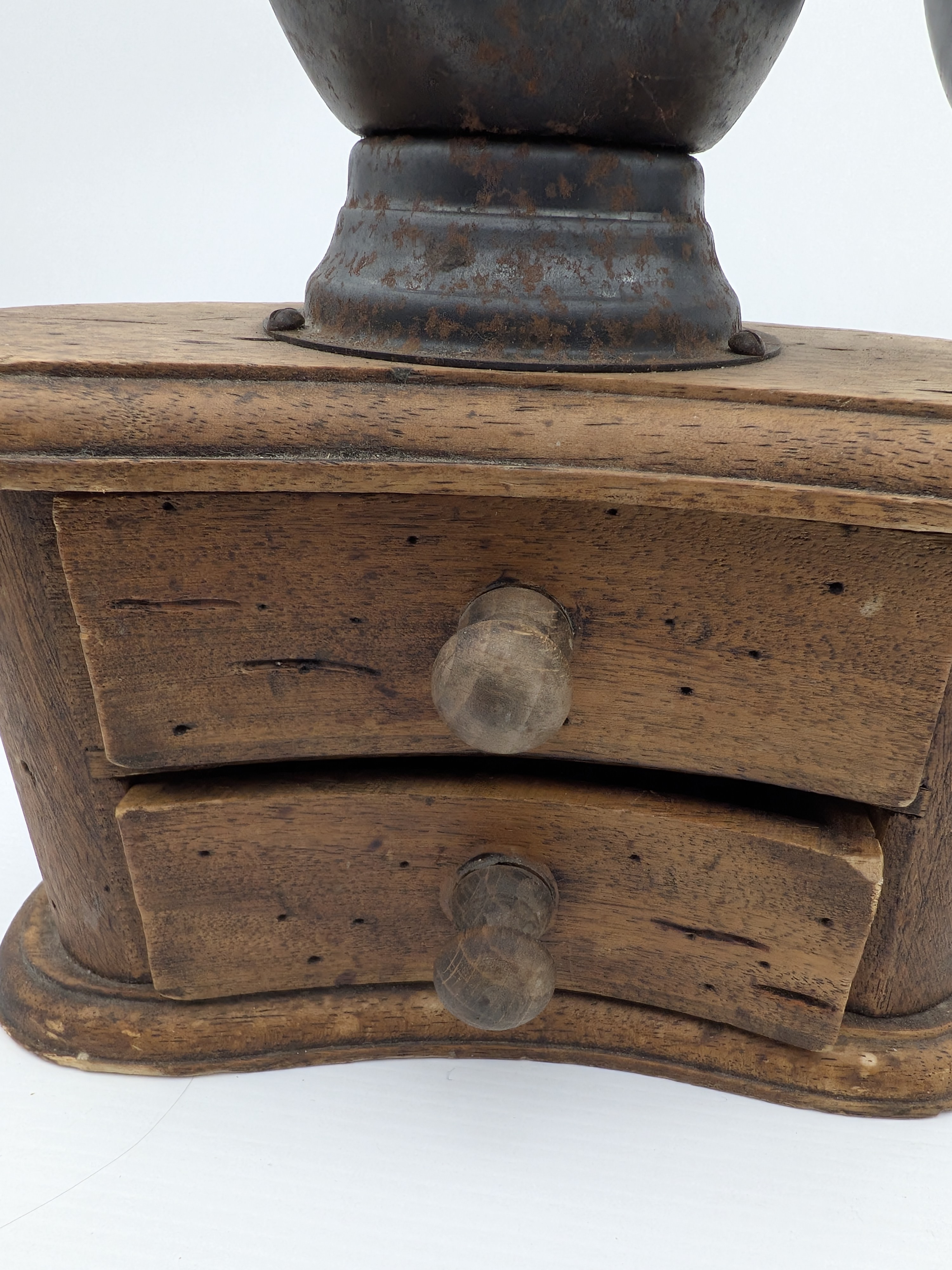 An antique wooden and cast iron hand-crank coffee grinder, featuring a robust iron grinding mechanism with a large flywheel and a solid wooden base housing two small collection drawers. - View 2