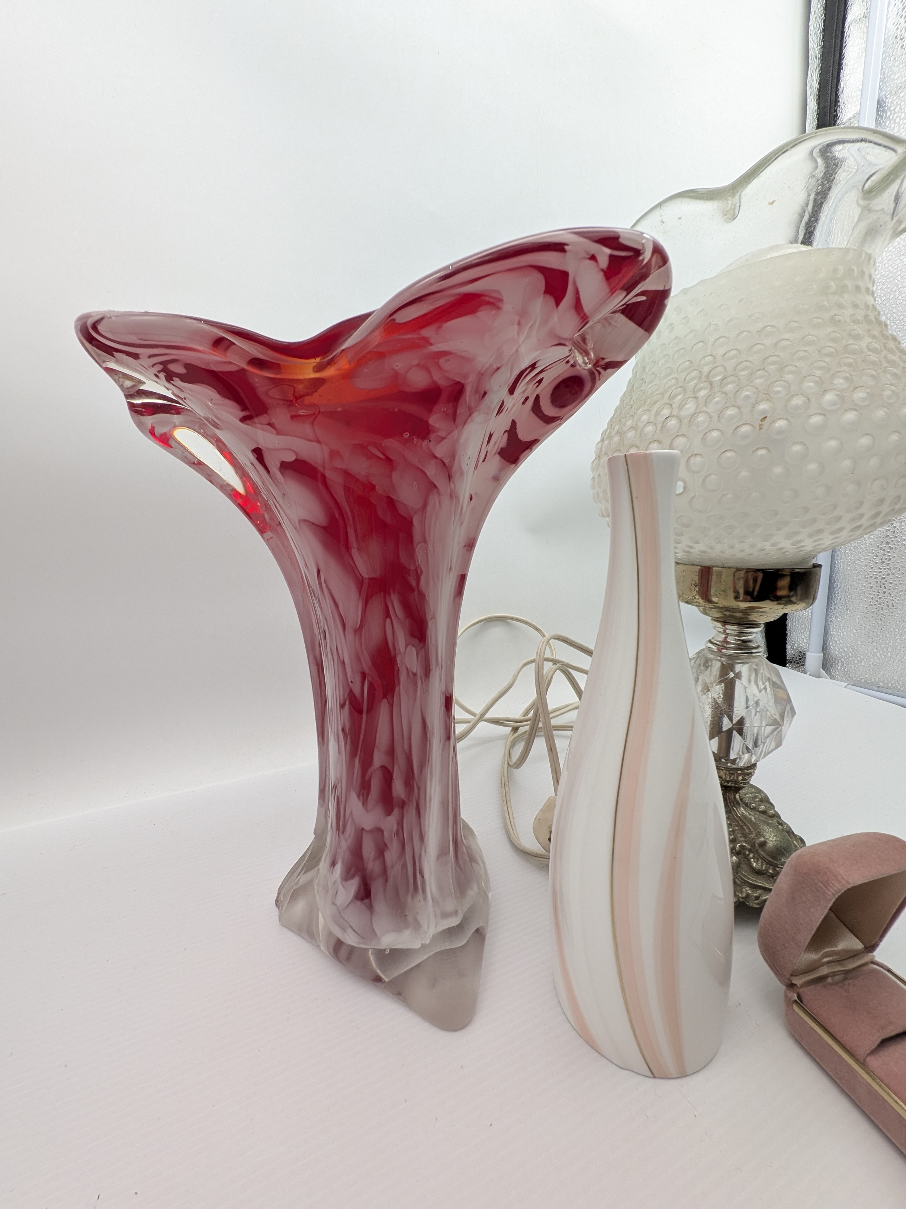 A charming collection of vintage decorative items, including a red art glass vase, a ceramic vase, a small hobnail glass table lamp, and a velvet jewellery box containing a silver-toned cameo necklace. - View 2