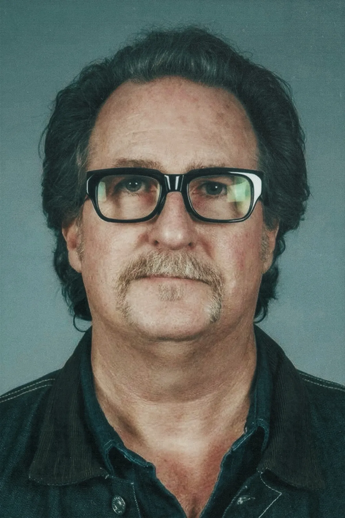 Casting director John Papsidera in a black leather jacket and glasses against a muted background