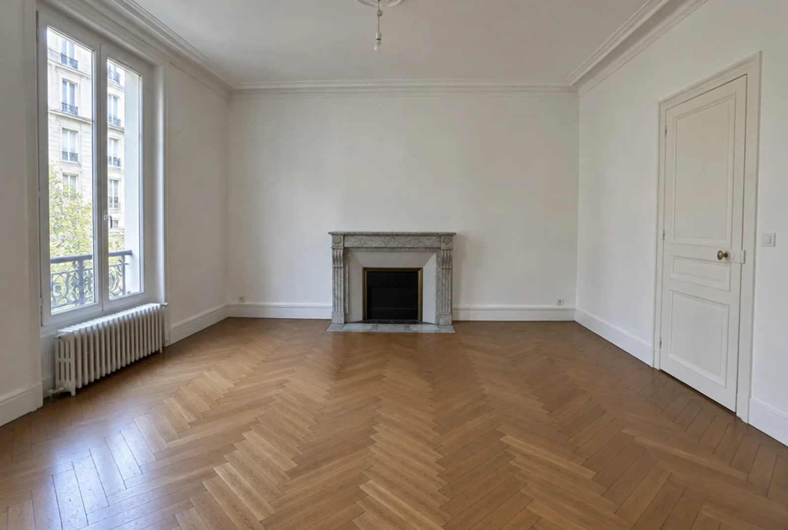 Pièce de départ, générée par IA : un salon vide avec parquet en point de Hongrie, cheminée en marbre, radiateur en fonte sous la fenêtre et porte à droite.