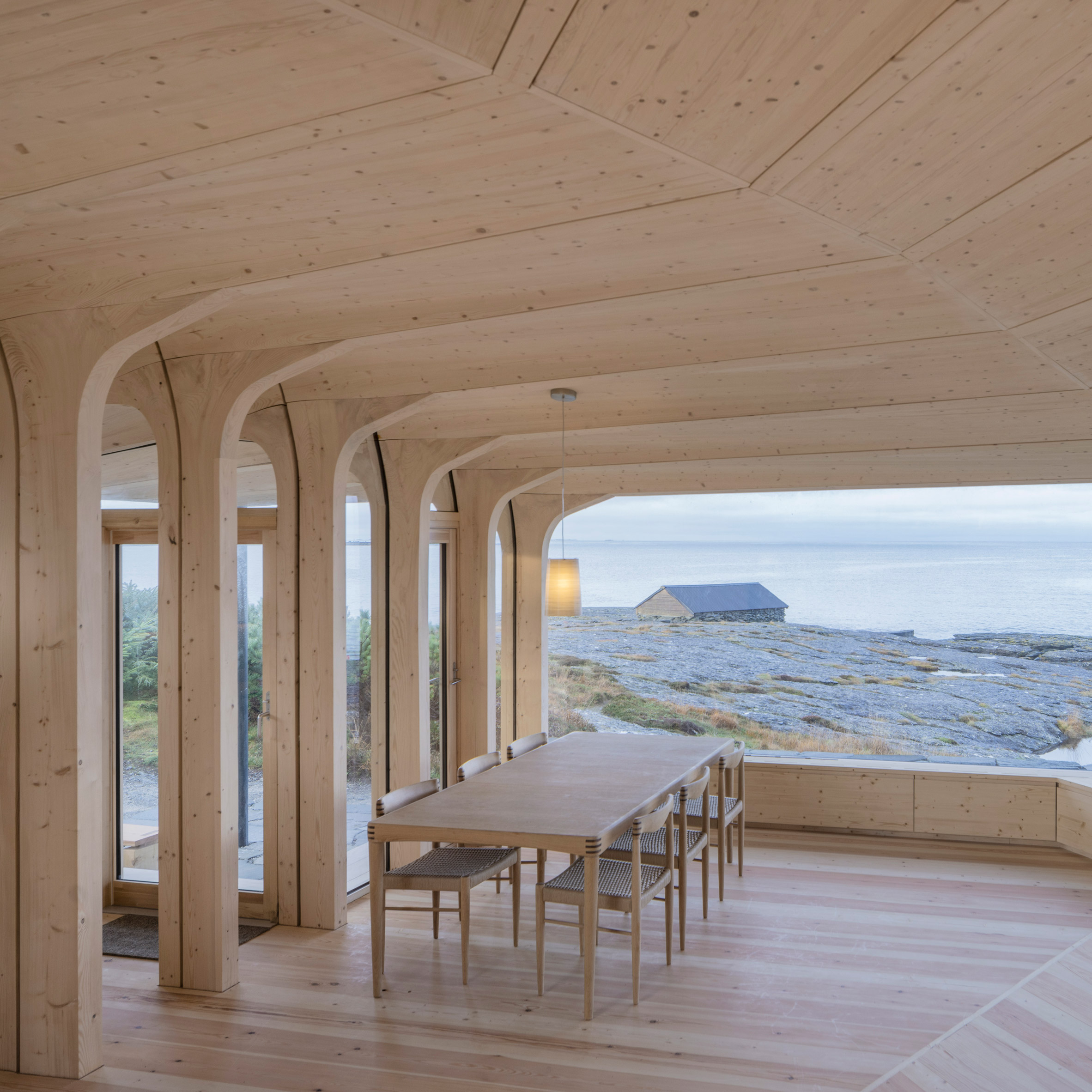Timber dining space overlooking the rocky coastline through a wide panoramic window