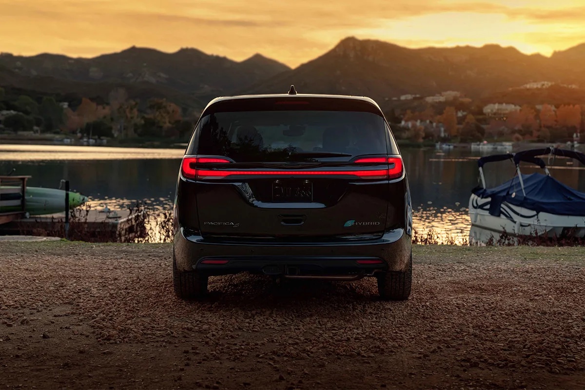 Chrysler Pacifica hybride 2026 vue arrière au coucher du soleil près d’un plan d’eau, mettant en valeur le design arrière, l’éclairage DEL et le caractère haut de gamme du modèle.