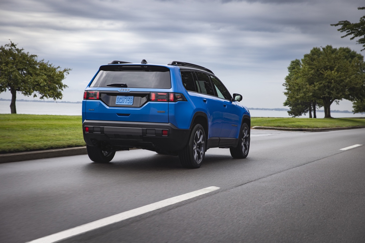 Vue arrière trois quarts du Jeep Cherokee hybride 2026 bleu sur route dégagée, montrant les feux arrière à DEL, le hayon et la silhouette dynamique du VUS.
