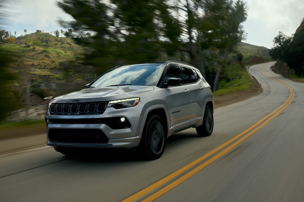 Jeep Compass 2023 gris vu de trois quarts avant en conduite sur route sinueuse, illustrant la stabilité, le confort de roulement et les performances du VUS compact Jeep.