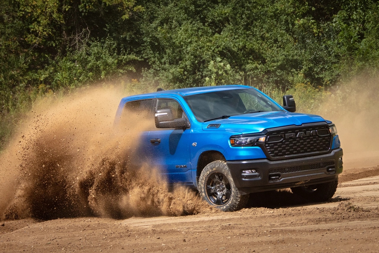 Ram 1500 2026 bleu en action sur chemin de terre, projetant de la poussière, illustrant la tenue de route, la traction et les performances hors route.