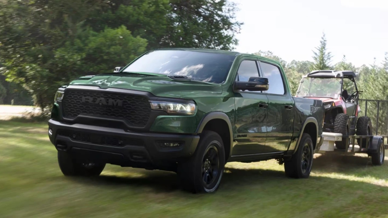 Ram 1500 2026 vert remorquant un véhicule récréatif sur une route gazonnée, démontrant la capacité de remorquage et la polyvalence du pickup pleine grandeur.