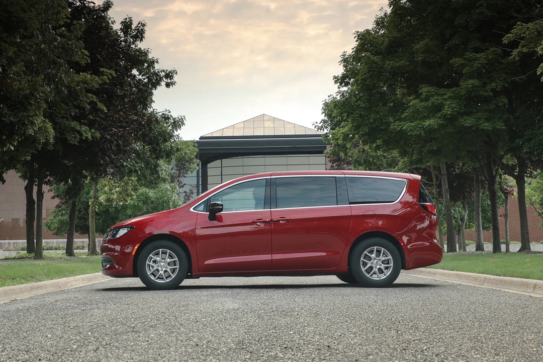 Vue de profil de la Chrysler Grand Caravan 2026 rouge stationnée en milieu urbain, mettant en évidence la longueur, les portes coulissantes et le design équilibré.