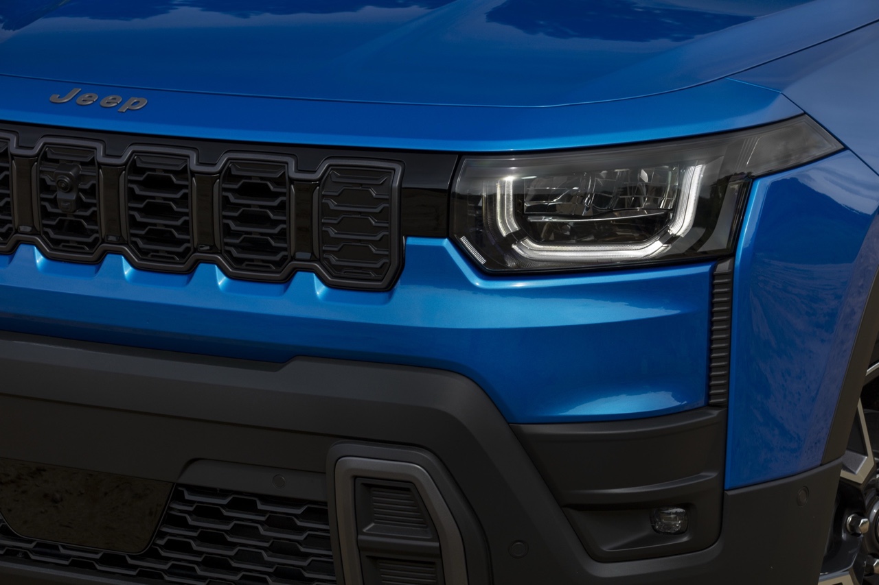 Gros plan de la calandre à sept fentes et du phare avant à DEL du Jeep Cherokee hybride 2026 bleu, soulignant le design modernisé et la signature lumineuse distinctive.