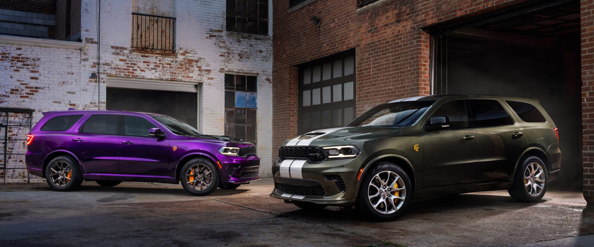 Deux Dodge Durango 2026 stationnés en milieu urbain industriel, l’un violet et l’autre vert kaki à bandes blanches, illustrant les versions sport et la personnalisation.