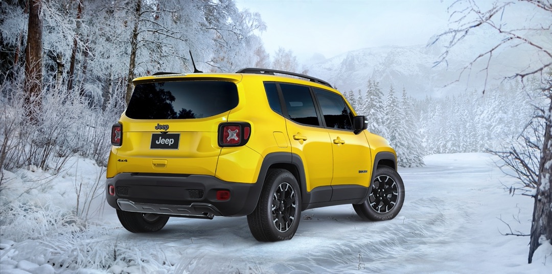 Jeep Renegade 2023 jaune vu arrière trois quarts sur route enneigée en forêt, mettant en valeur le format compact, la traction intégrale et les capacités hivernales du VUS sous-compact.