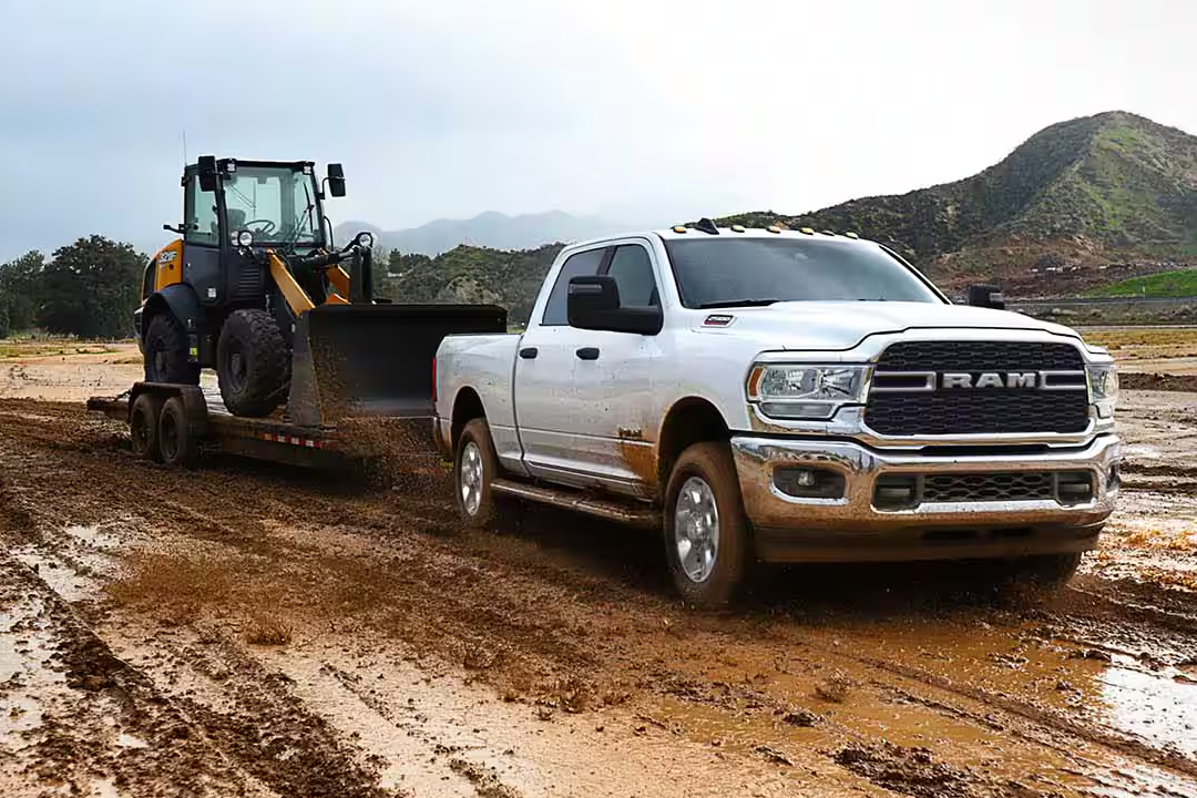 Vue 3/4 avant et latérale Du RAM 2500 2024 dans la boue avec remorque et tracteur